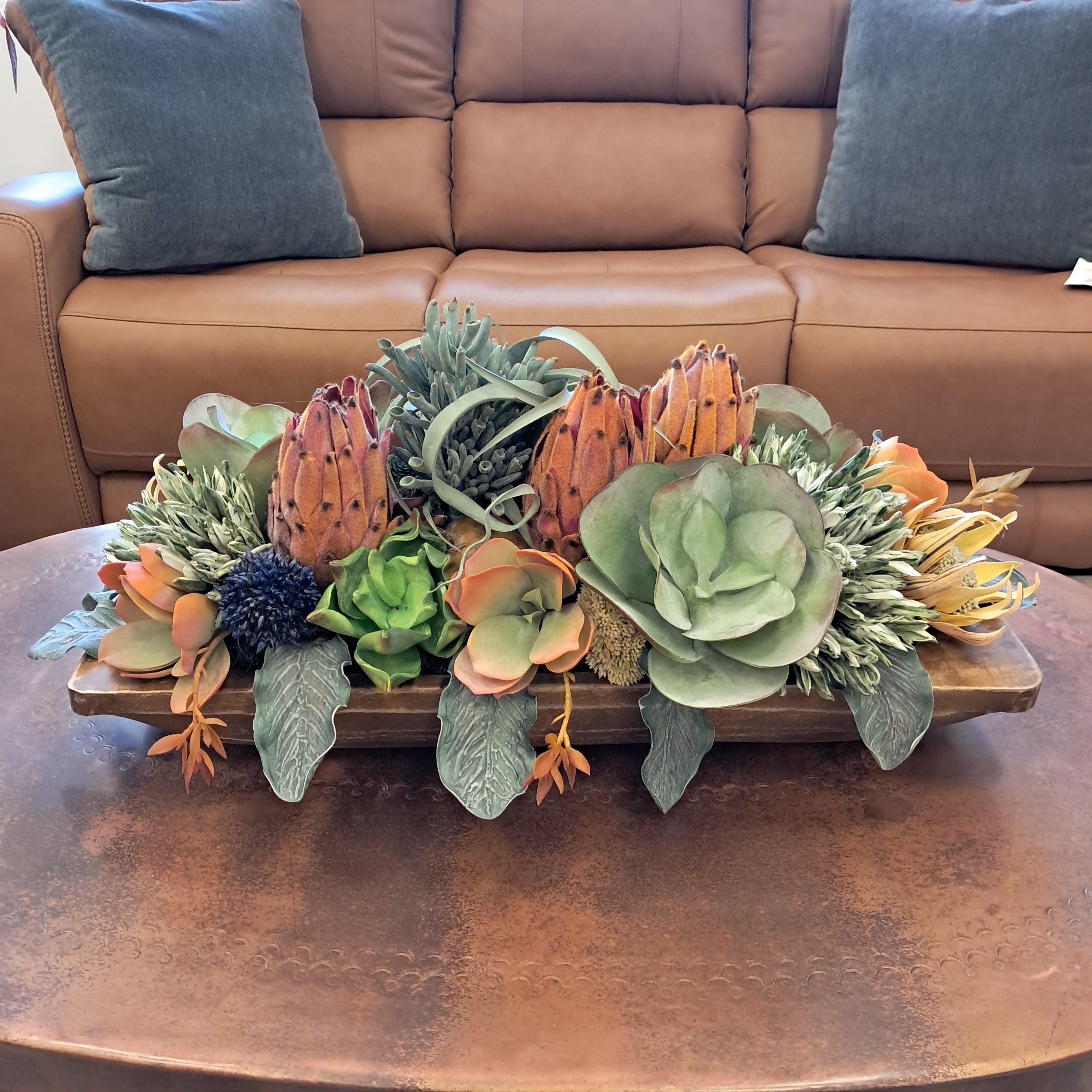 Decorative wall piece with succulents and cacti on a brown leather sofa.