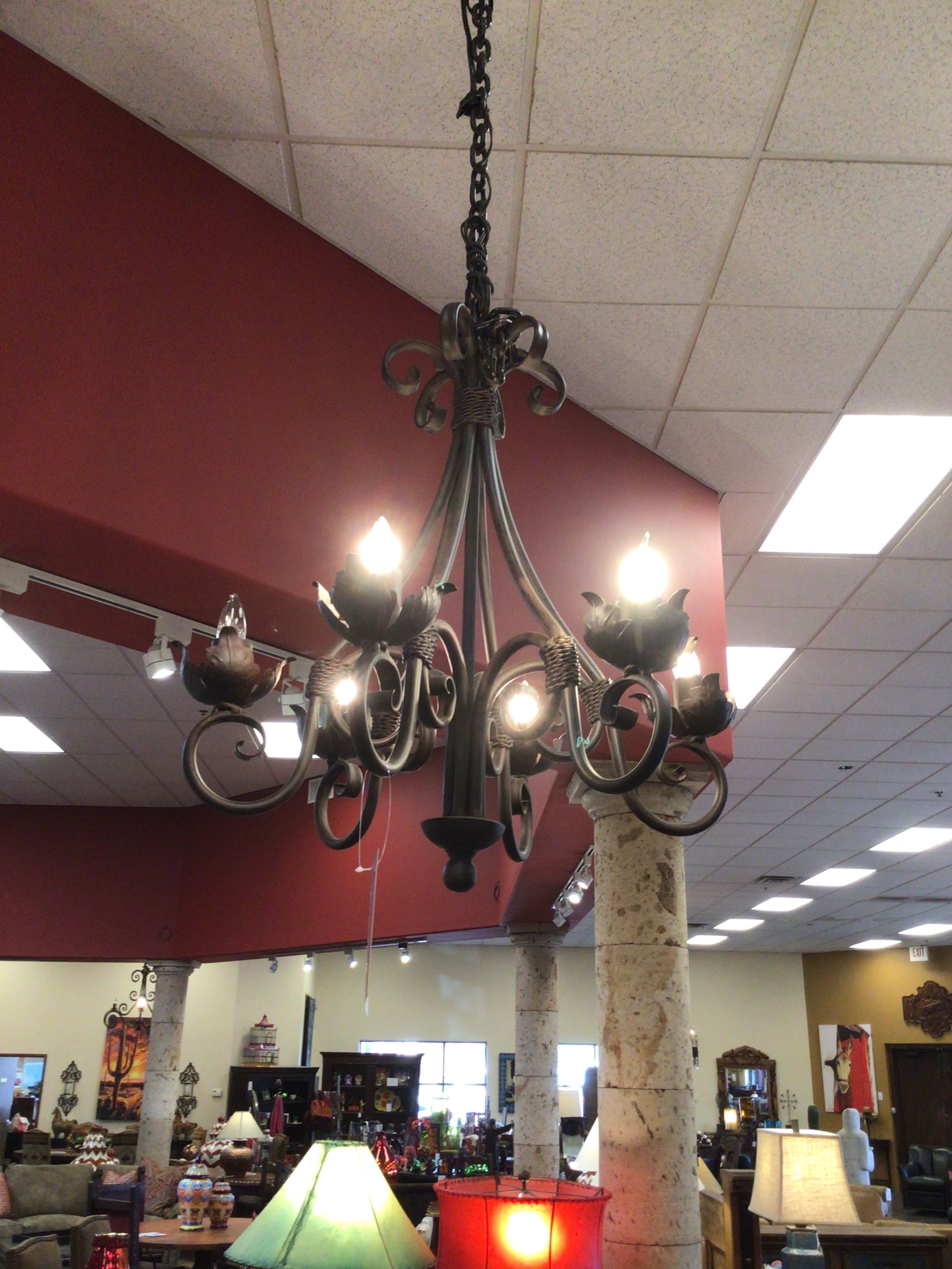 Decorative chandelier hanging in a store with red walls and ceiling lights.