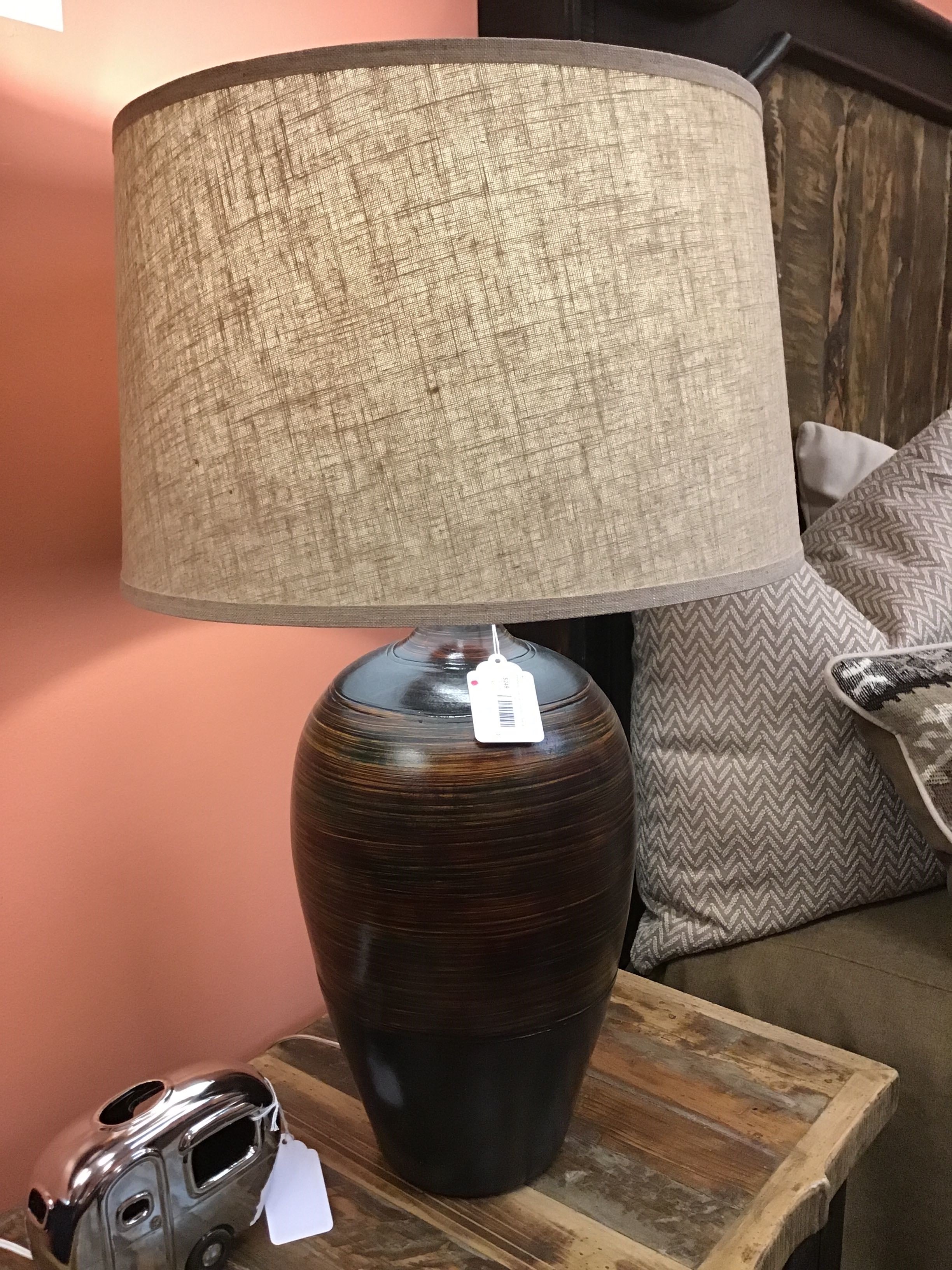 Table lamp with a textured beige shade on a wooden table against a pink wall.