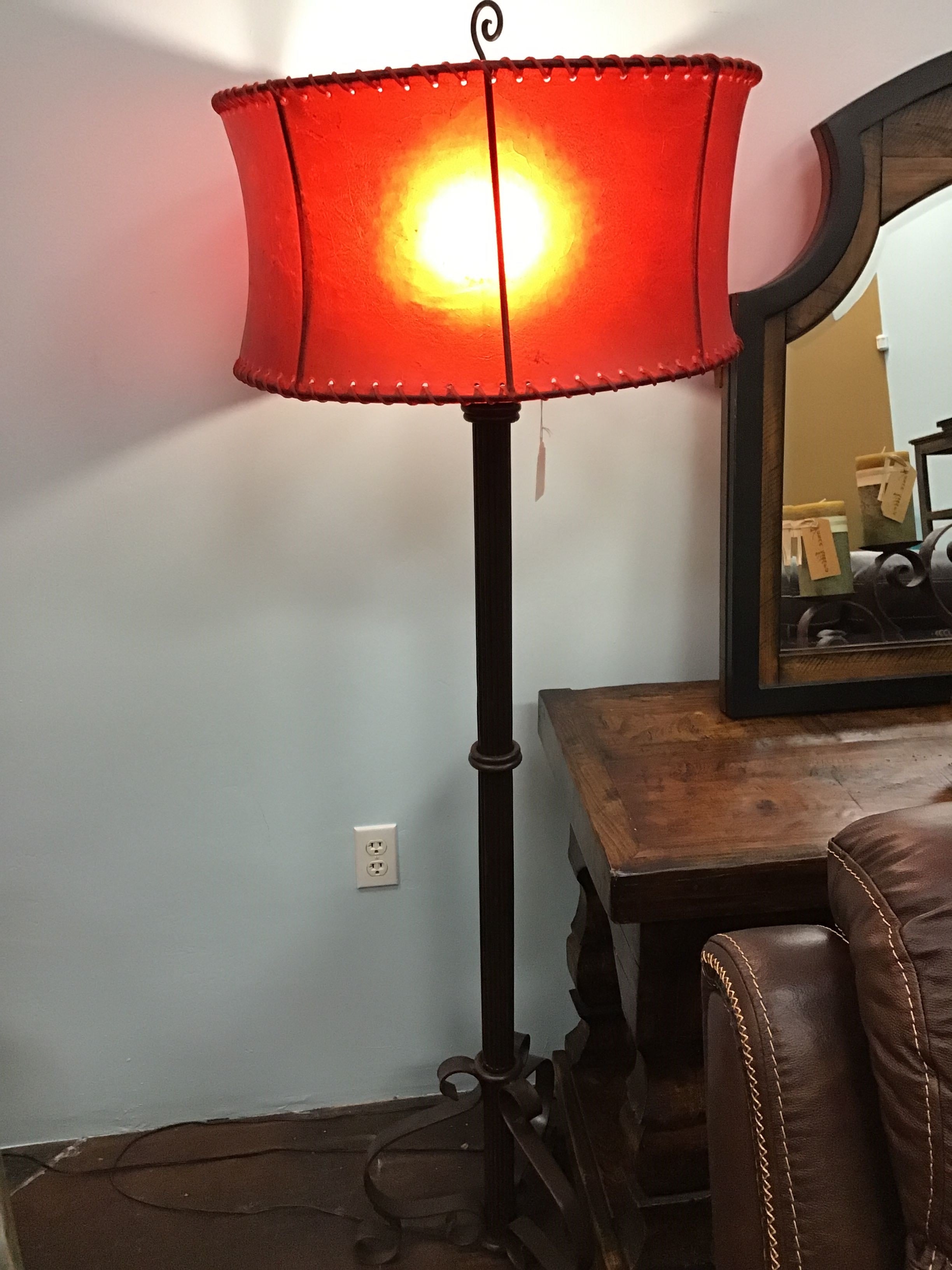 Floor lamp with a red shade in a room with a mirror and furniture.