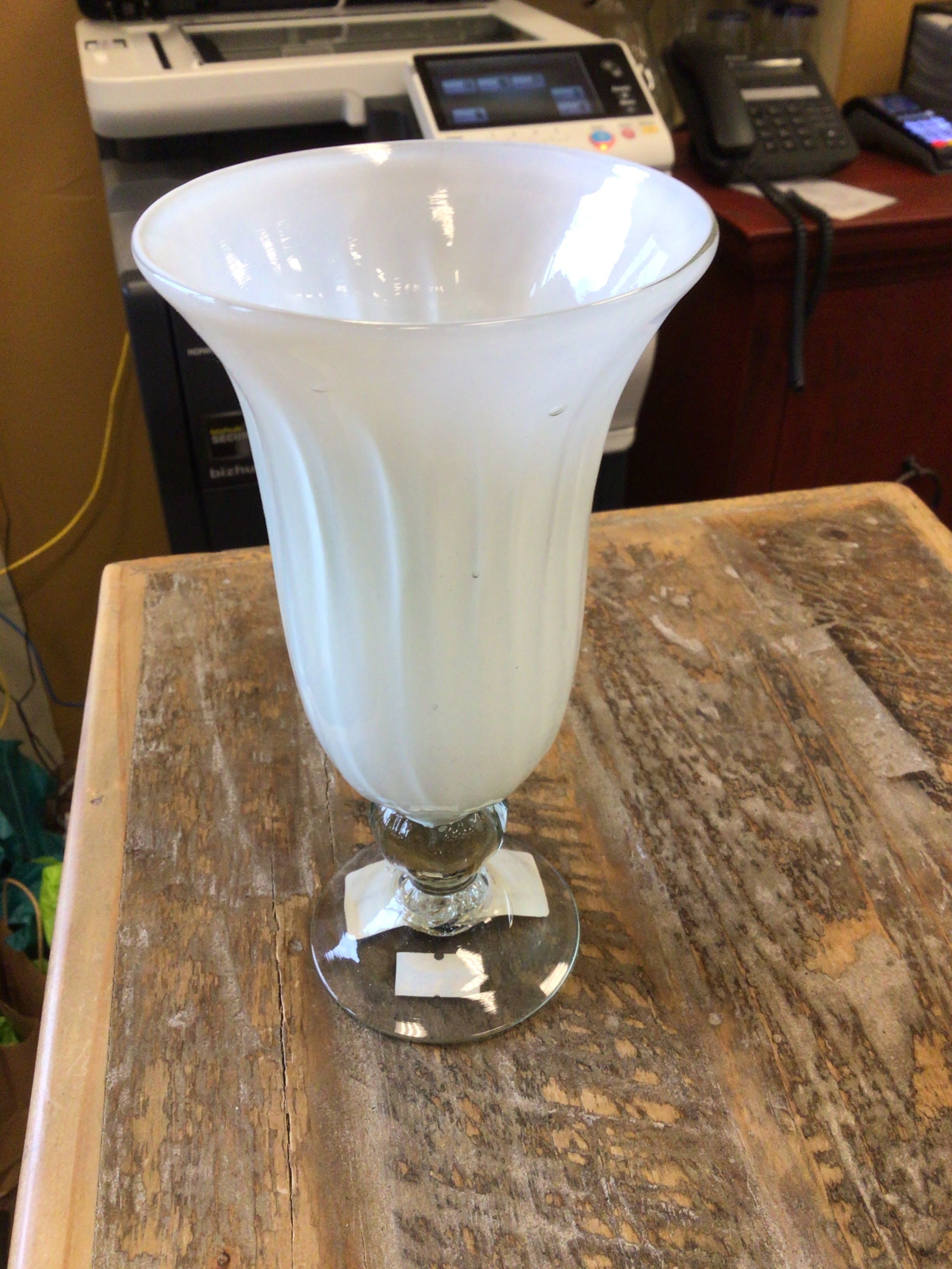 White glass vase on a wooden surface with office equipment in the background