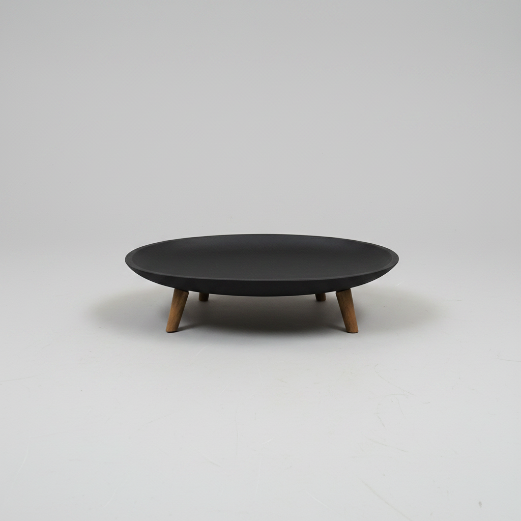 A minimalist oval coffee table with a matte black top and four tapered wooden legs, photographed on a seamless light gray studio background.