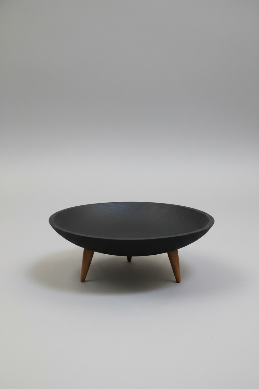 A modern black ceramic bowl with three tapered wooden legs, photographed against a neutral gray studio background.