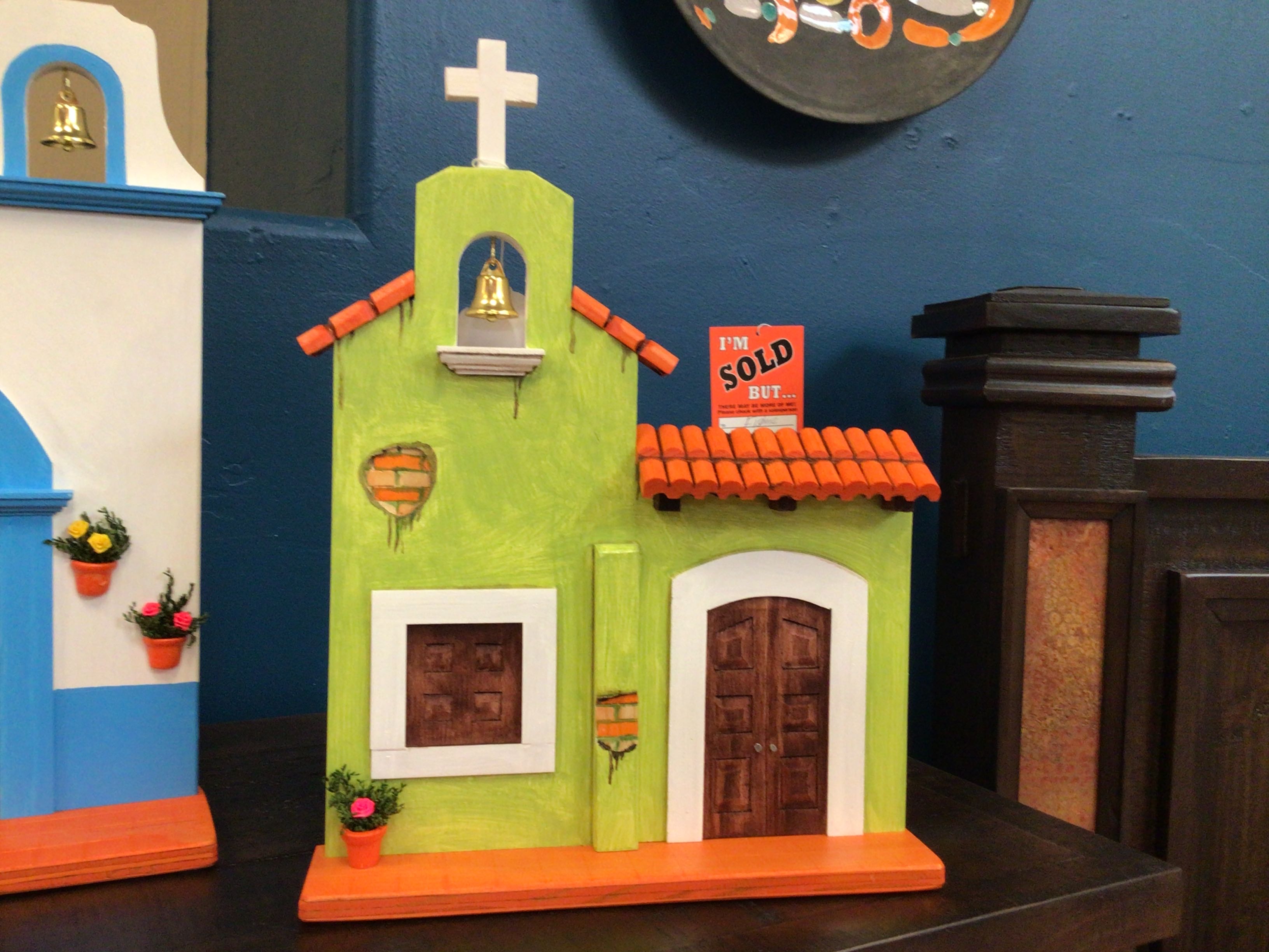 Model of a green church with an orange roof and a 'SOLD' sign on a blue wall.