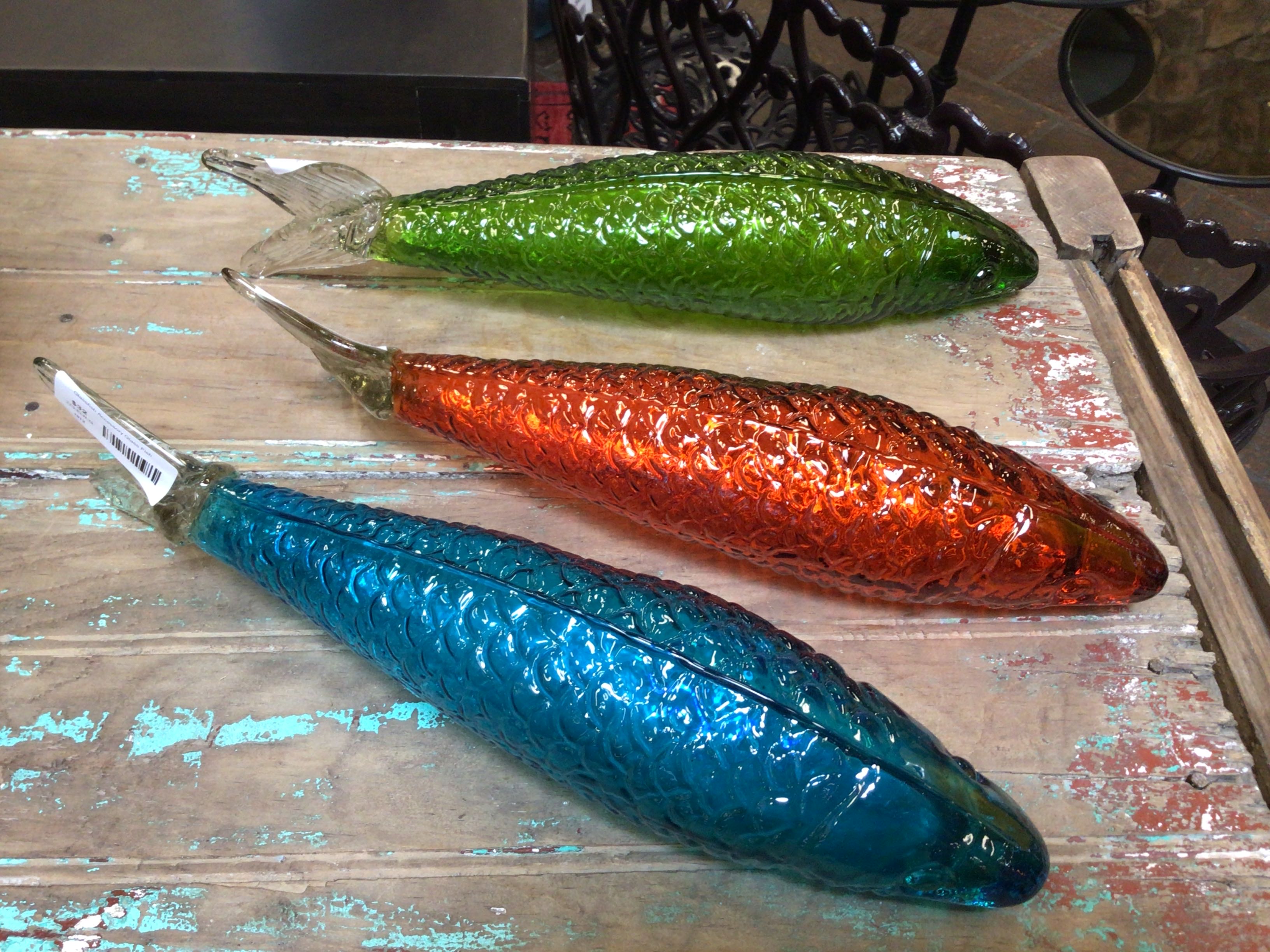 Three glass fish-shaped objects on a rustic wooden surface