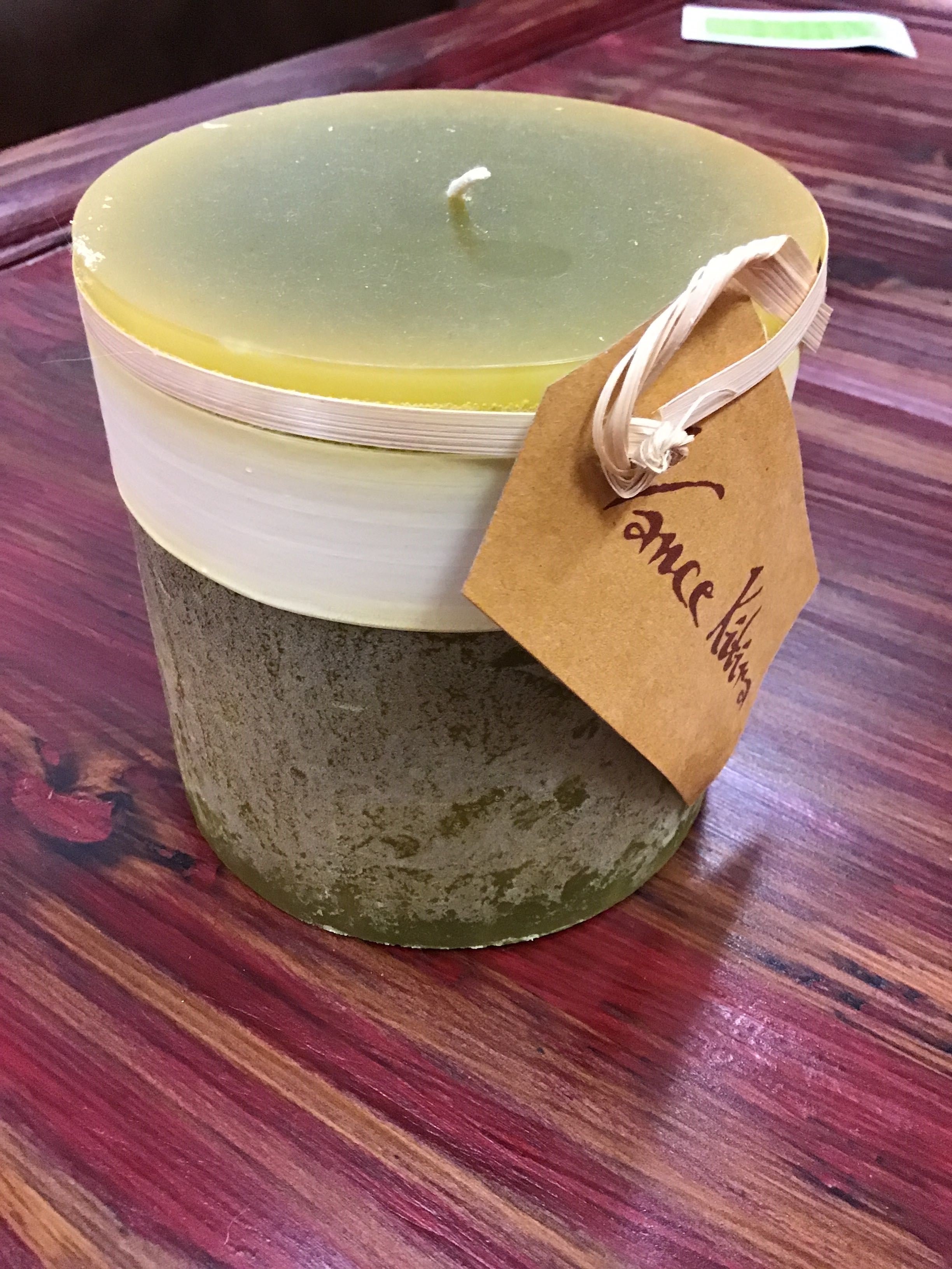 Candle in a textured container with a brown tag on a wooden surface