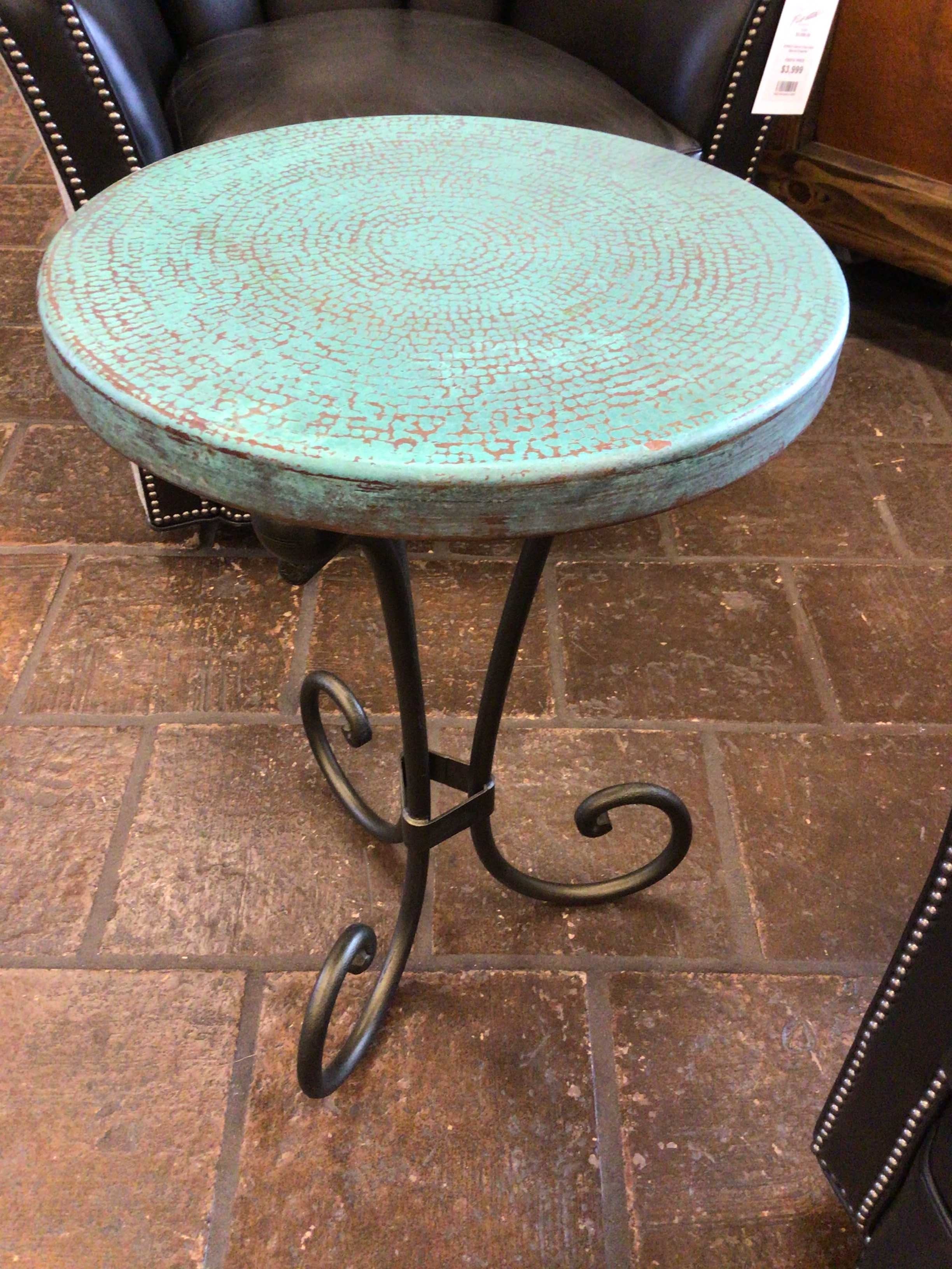 Small round turquoise table with decorative legs on a tiled floor