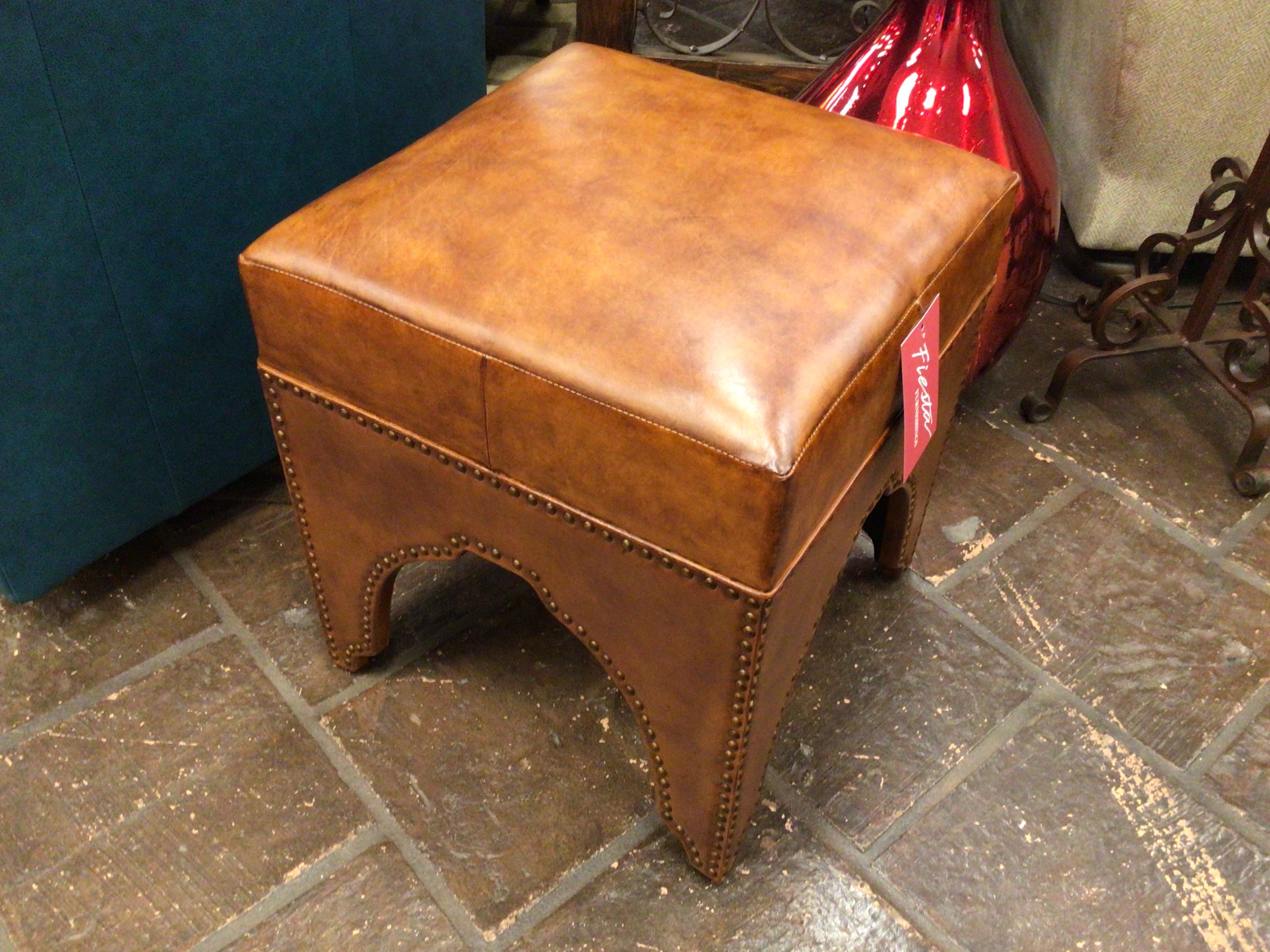Brown leather ottoman on a stone floor with a red bag in the background