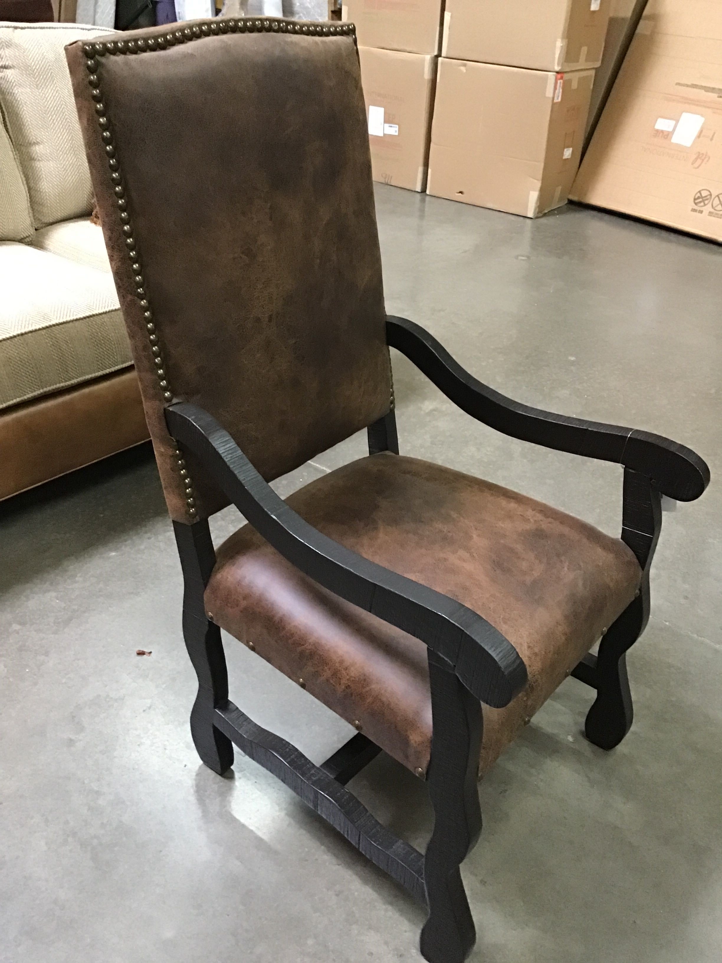 Brown leather armchair with black wooden frame in a warehouse setting