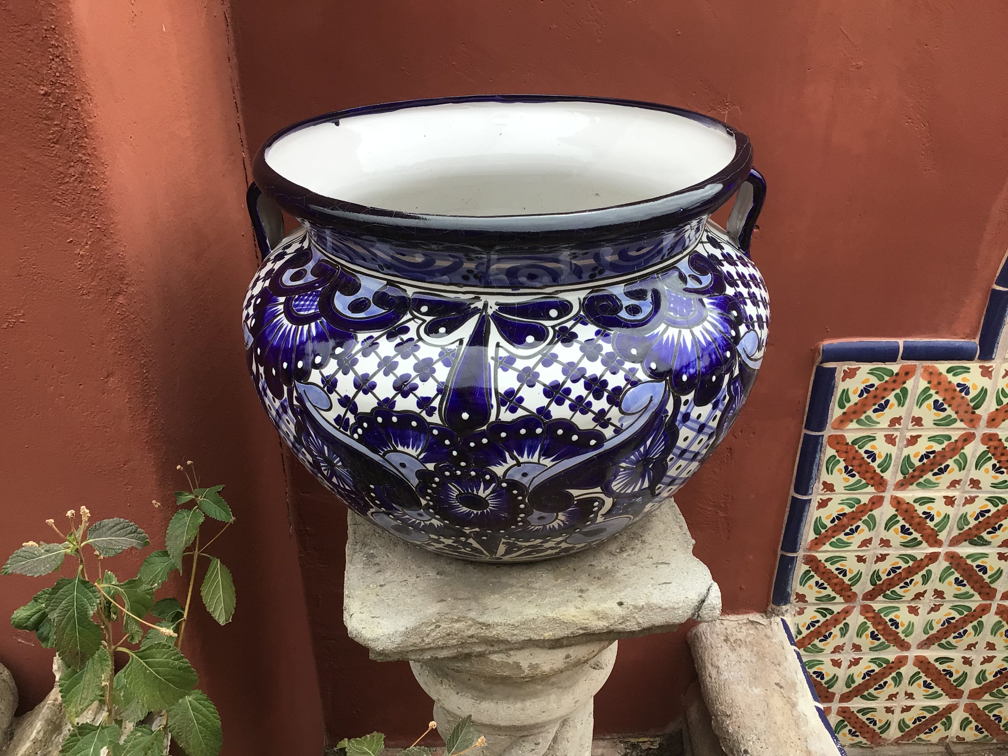Decorative blue and white ceramic pot on a stone pedestal against a red wall.