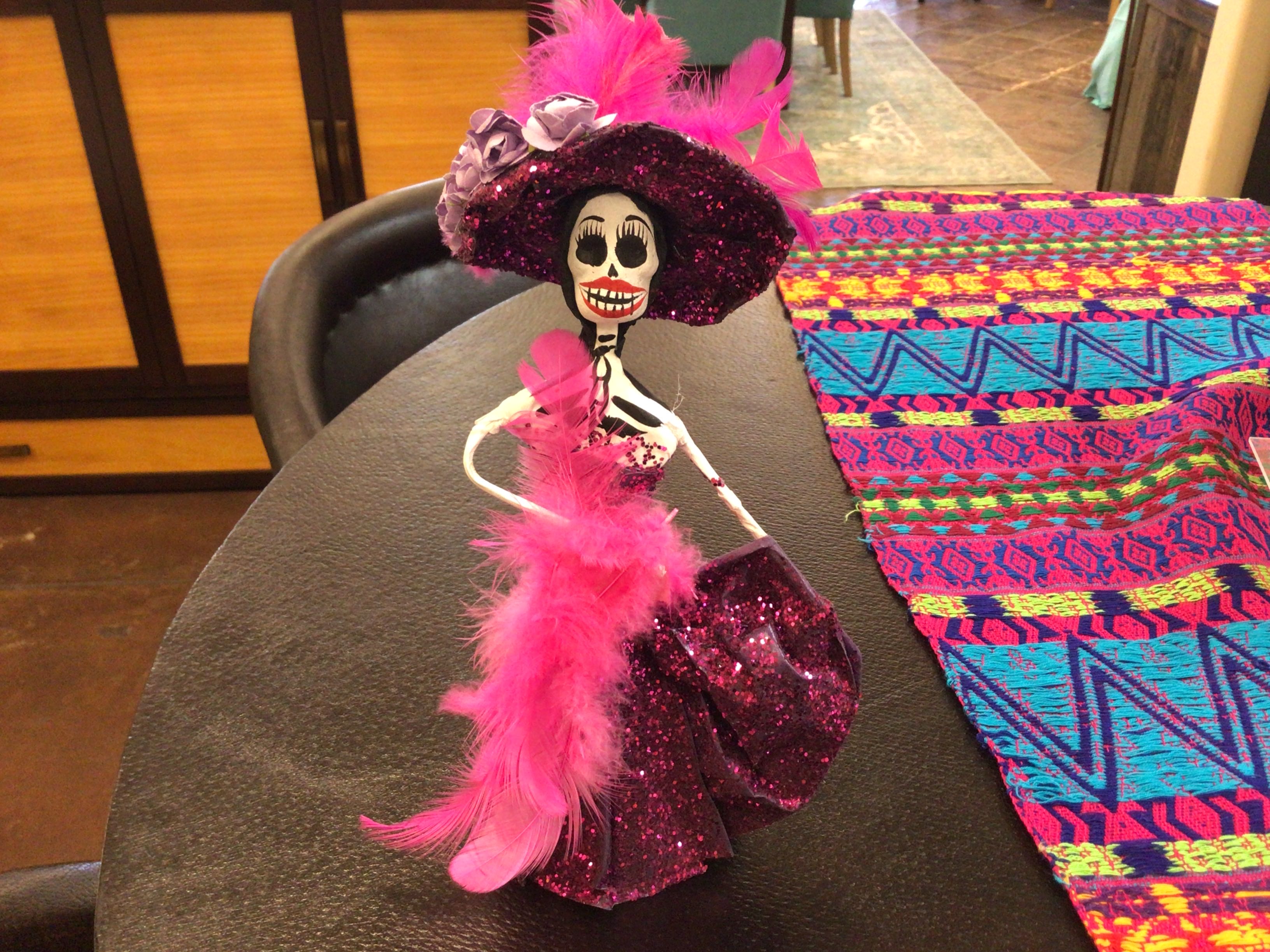 Decorative skeleton figure with pink feathers and sparkles on a table with a colorful patterned cloth.