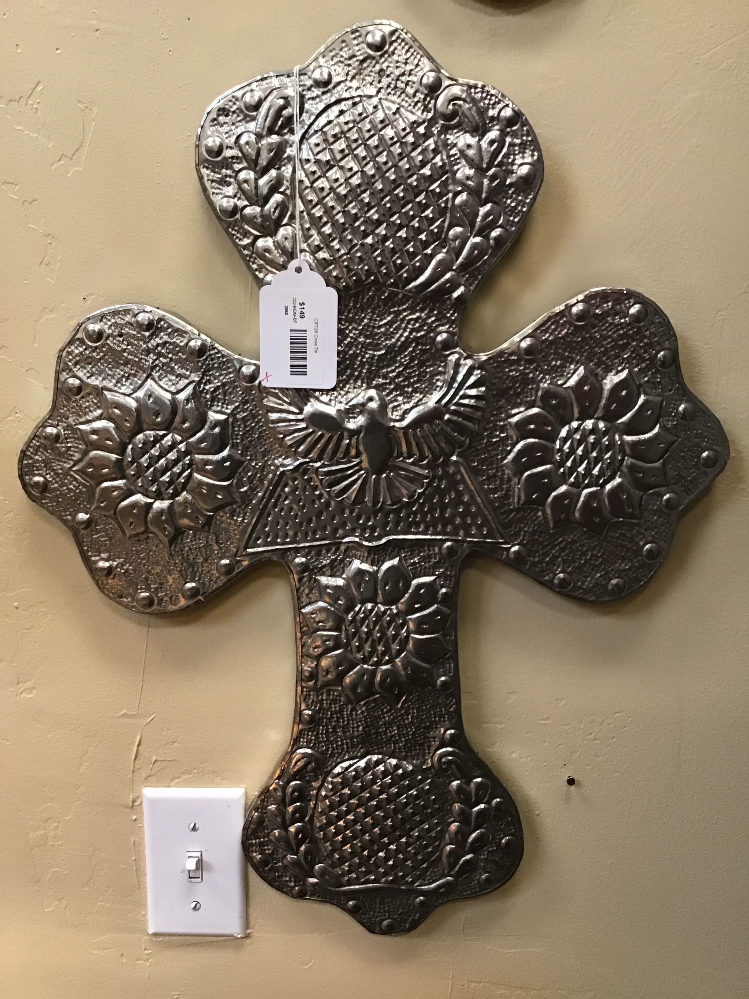 Decorative metal cross on a beige wall with a light switch.