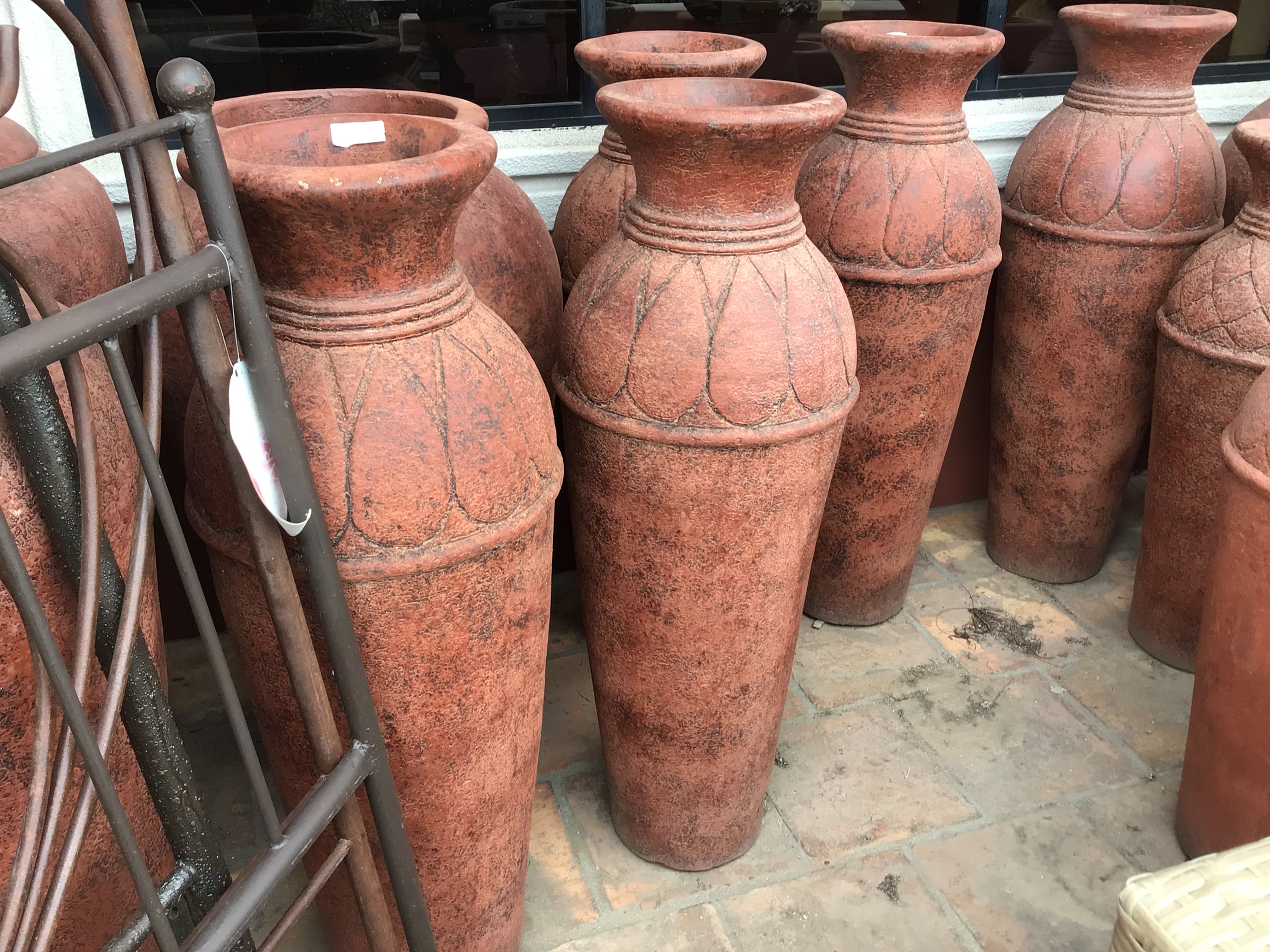 Row of terracotta vases on a stone floor with a metal stand.