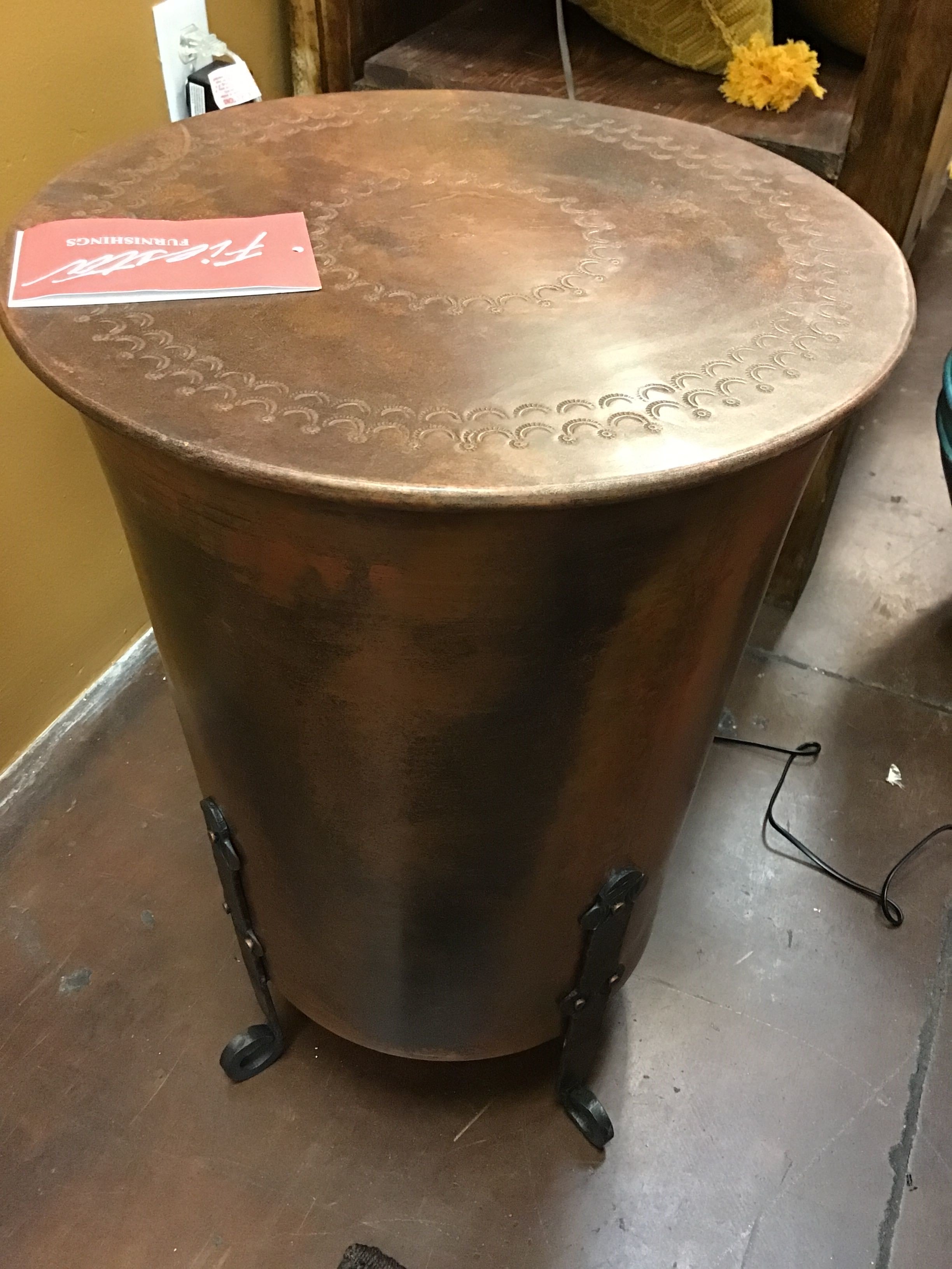 Bronze cylindrical table with engraved patterns on a wooden floor.
