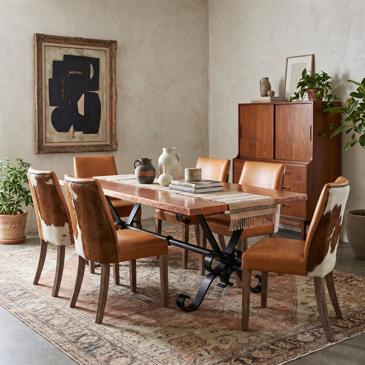 A dining room set featuring a rectangular wooden table with a rustic stone-look top and black metal base, surrounded by six chairs with brown leather and cowhide upholstery, set on a patterned area rug in a styled room.