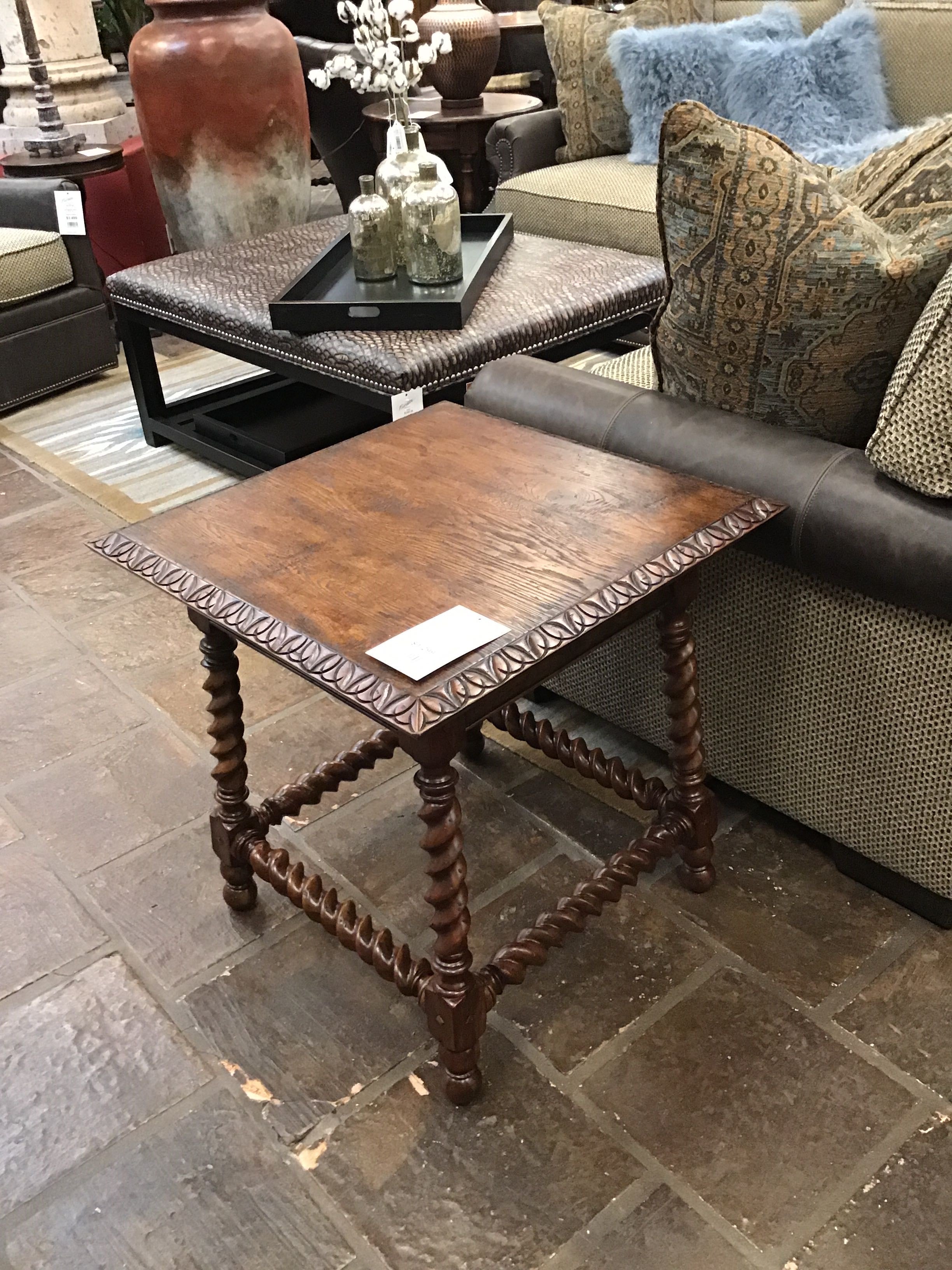 Wooden side table in a furniture store setting with a sofa and decorative pillows.
