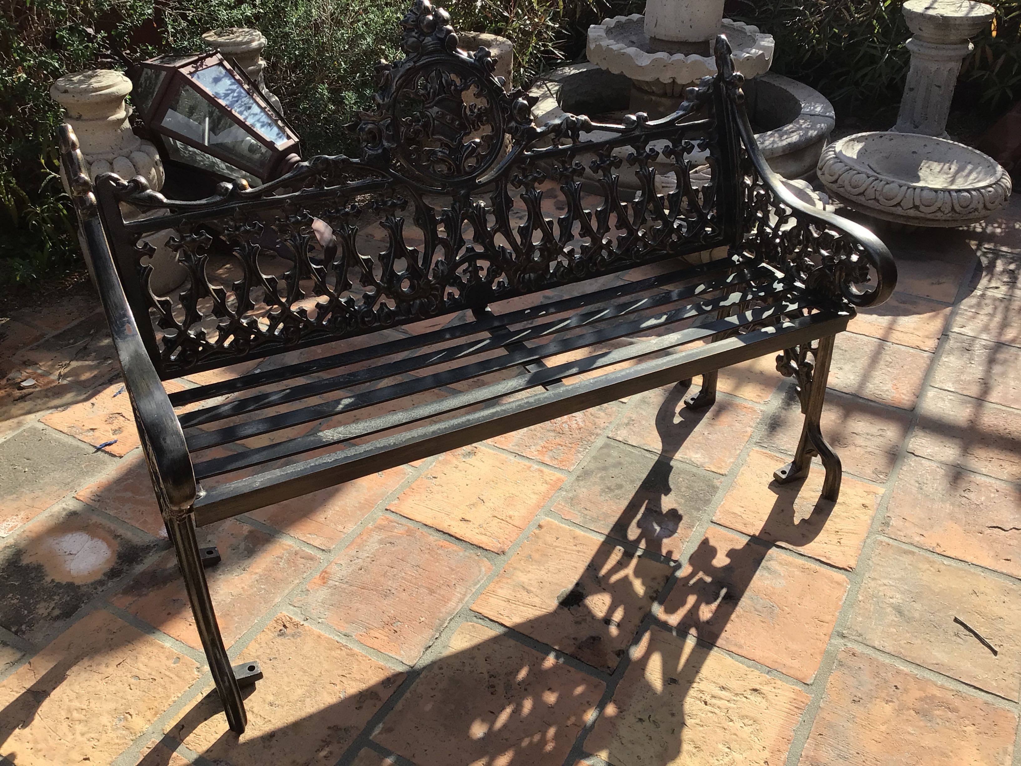 Decorative black metal bench on a brick patio with garden elements in the background
