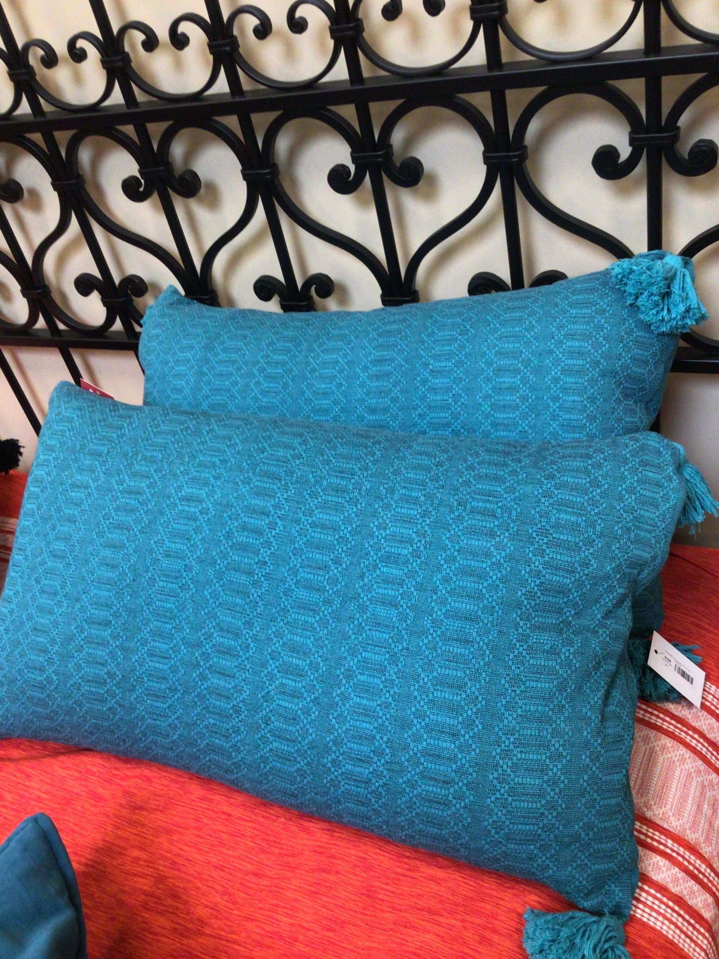 Two blue textured pillows on a red surface with a decorative metal headboard in the background.