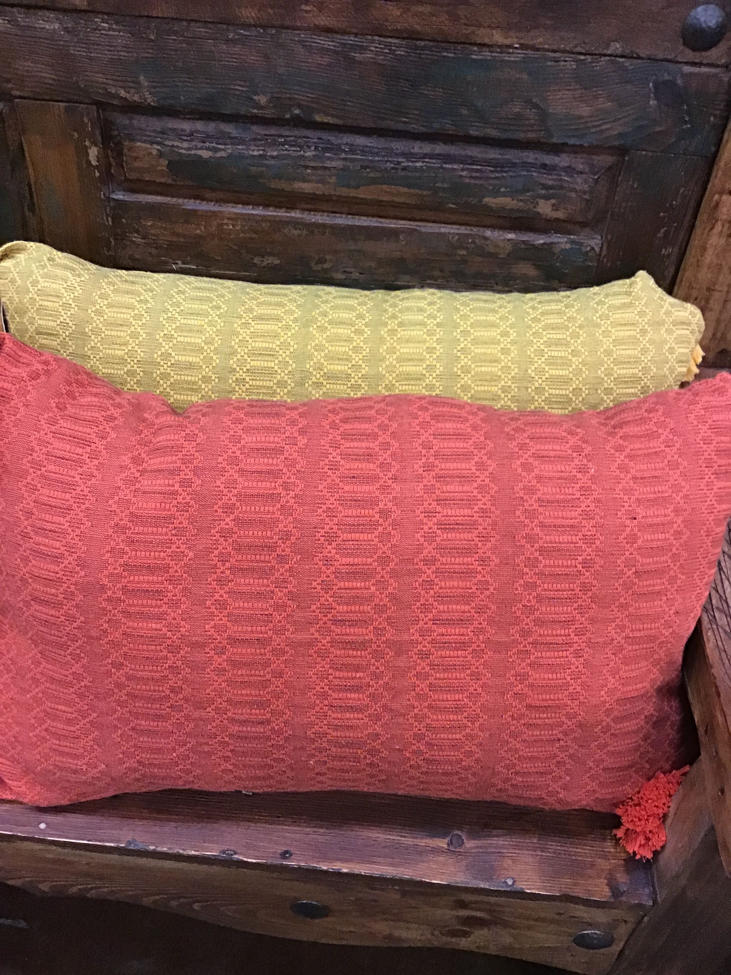 Two textured pillows, one yellow and one red, on a wooden surface.
