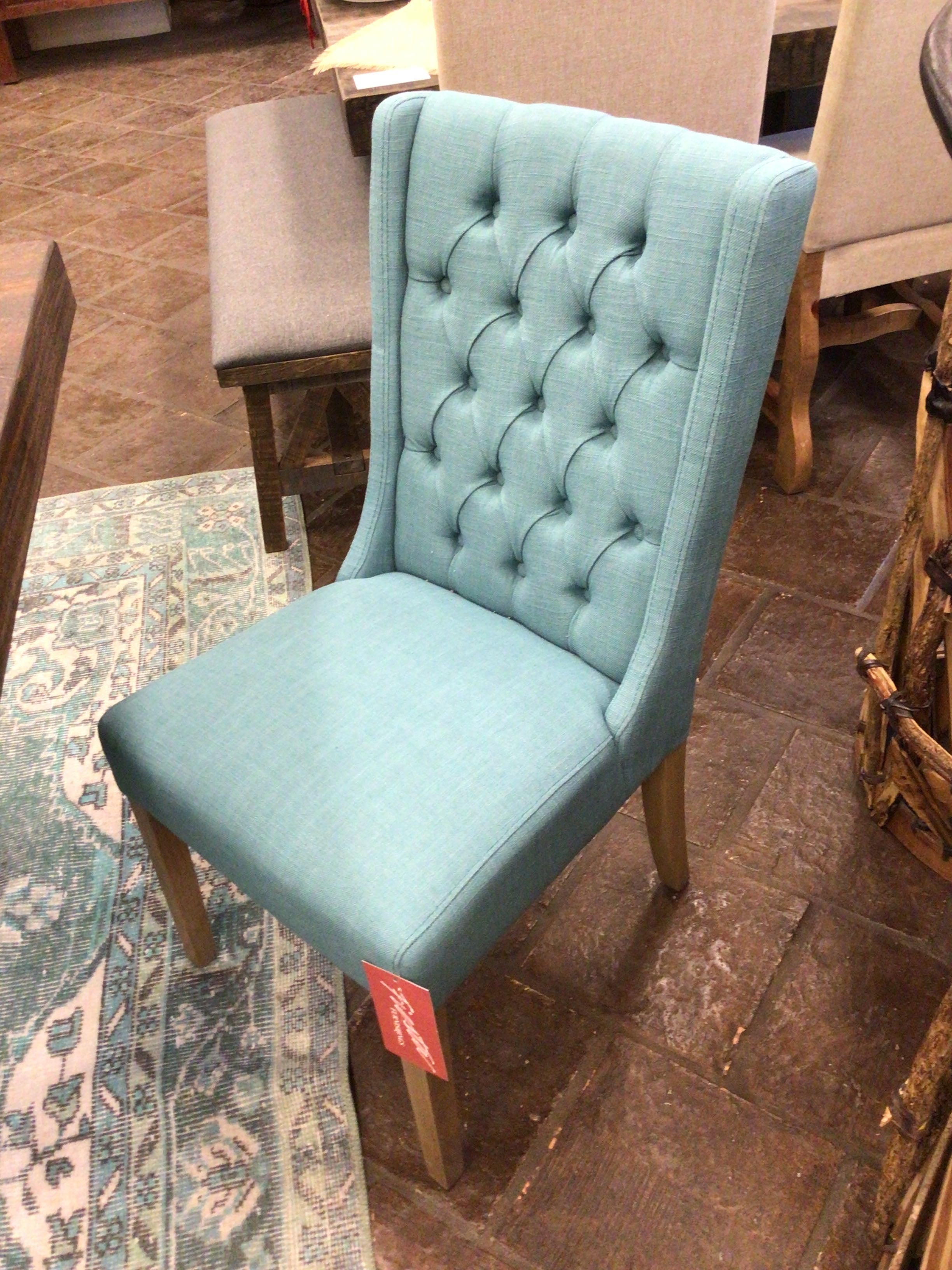 Teal upholstered chair with a tufted backrest on a wooden floor.