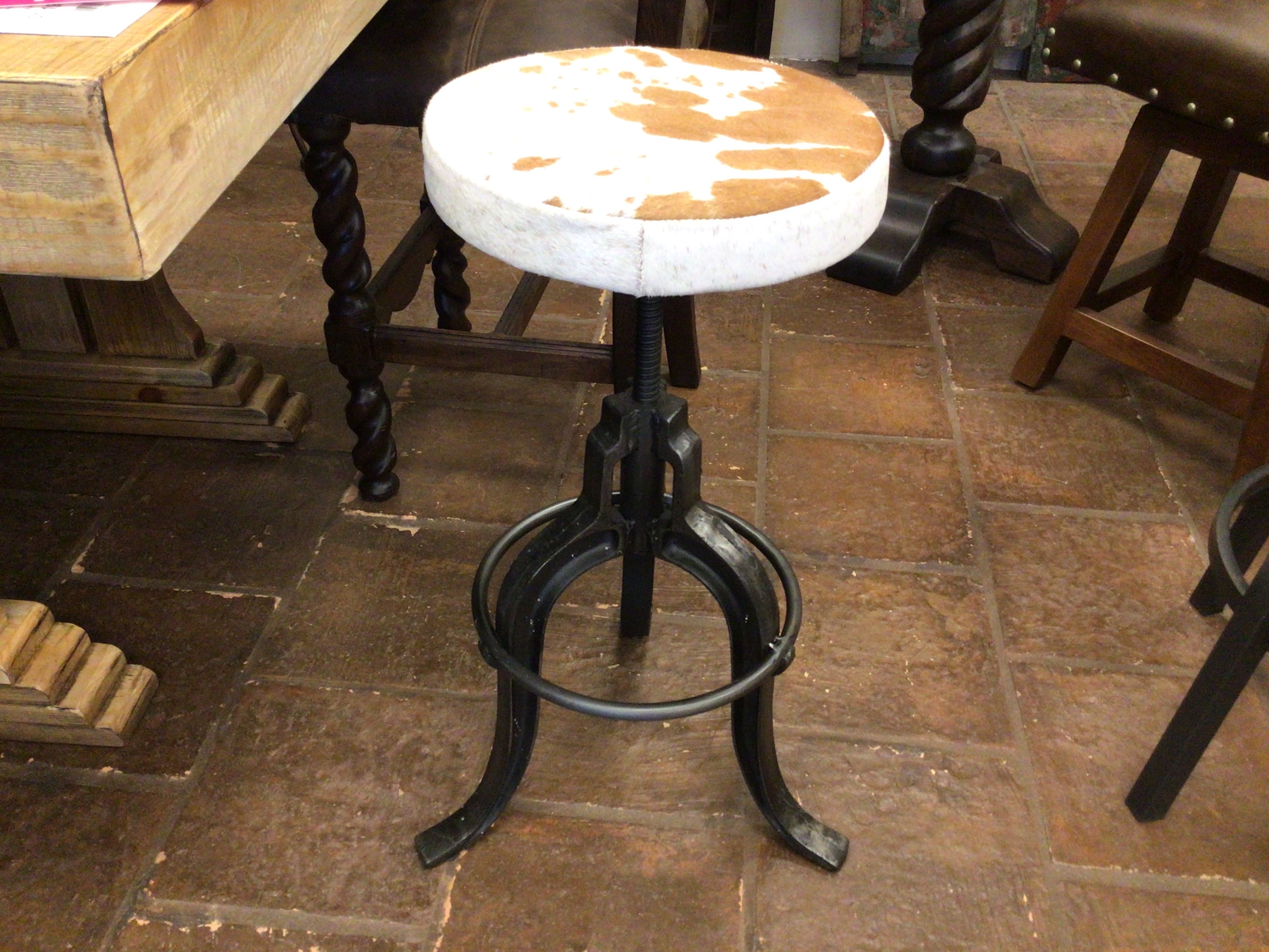 Bar stool with a white cushioned seat on a tiled floor in a rustic setting.