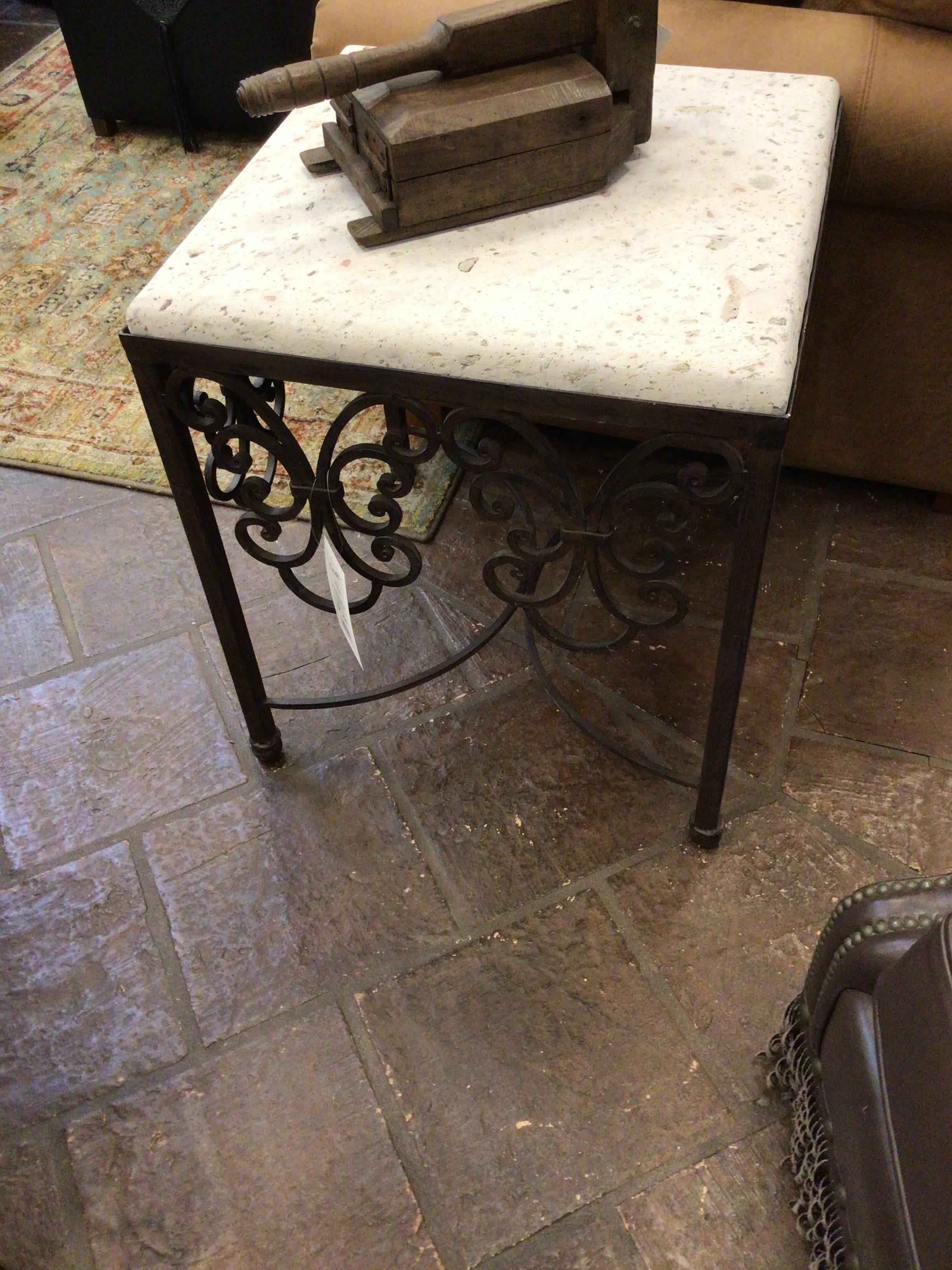 Small side table with marble top and decorative metal base on a tiled floor.