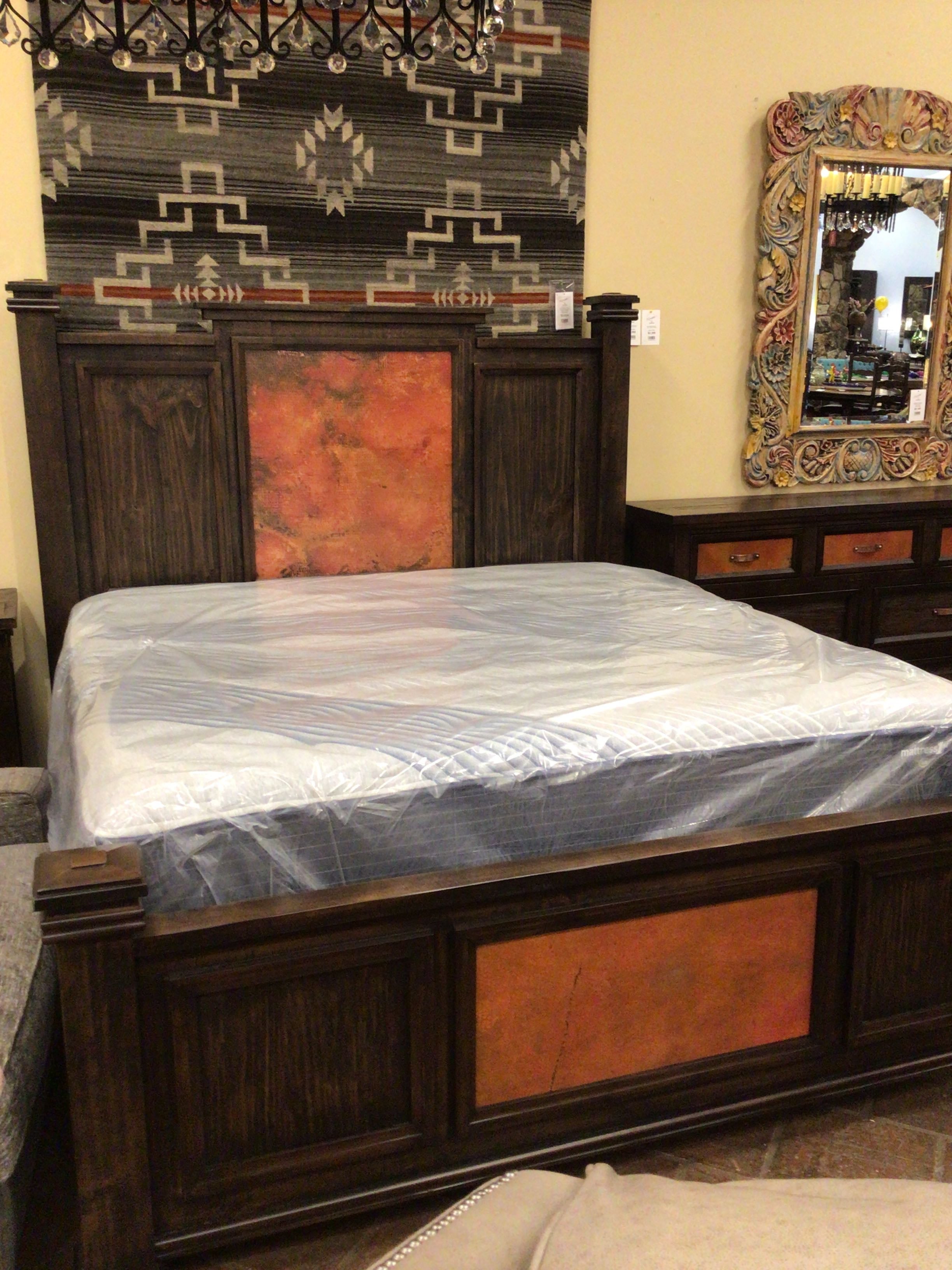 Wooden bed with red accents in a room setting with a rug and mirror.