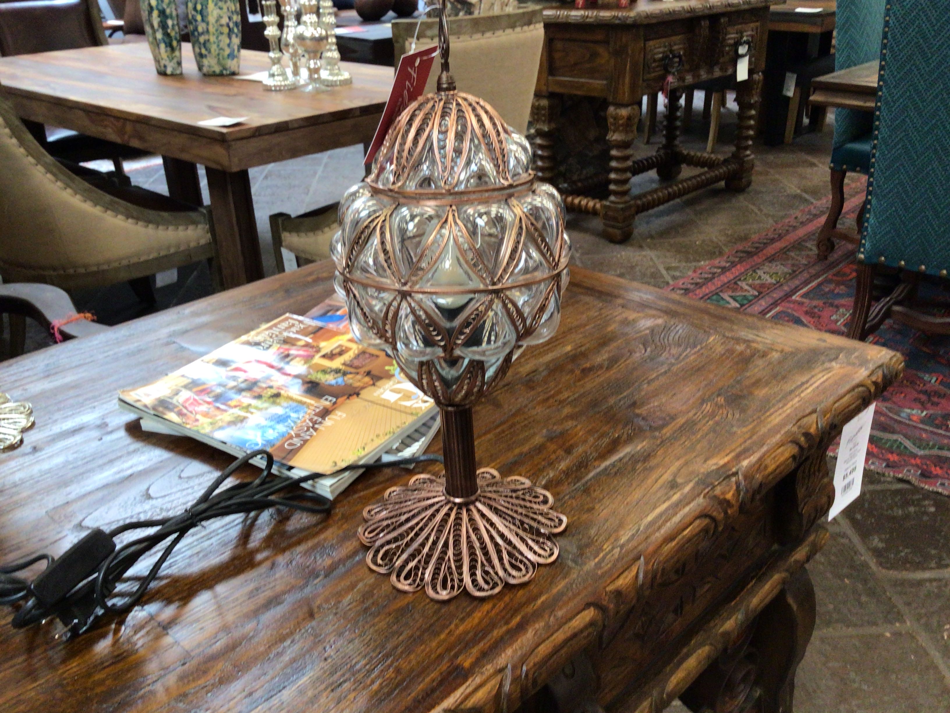 Decorative lamp on a wooden table with a magazine underneath, in an indoor setting.