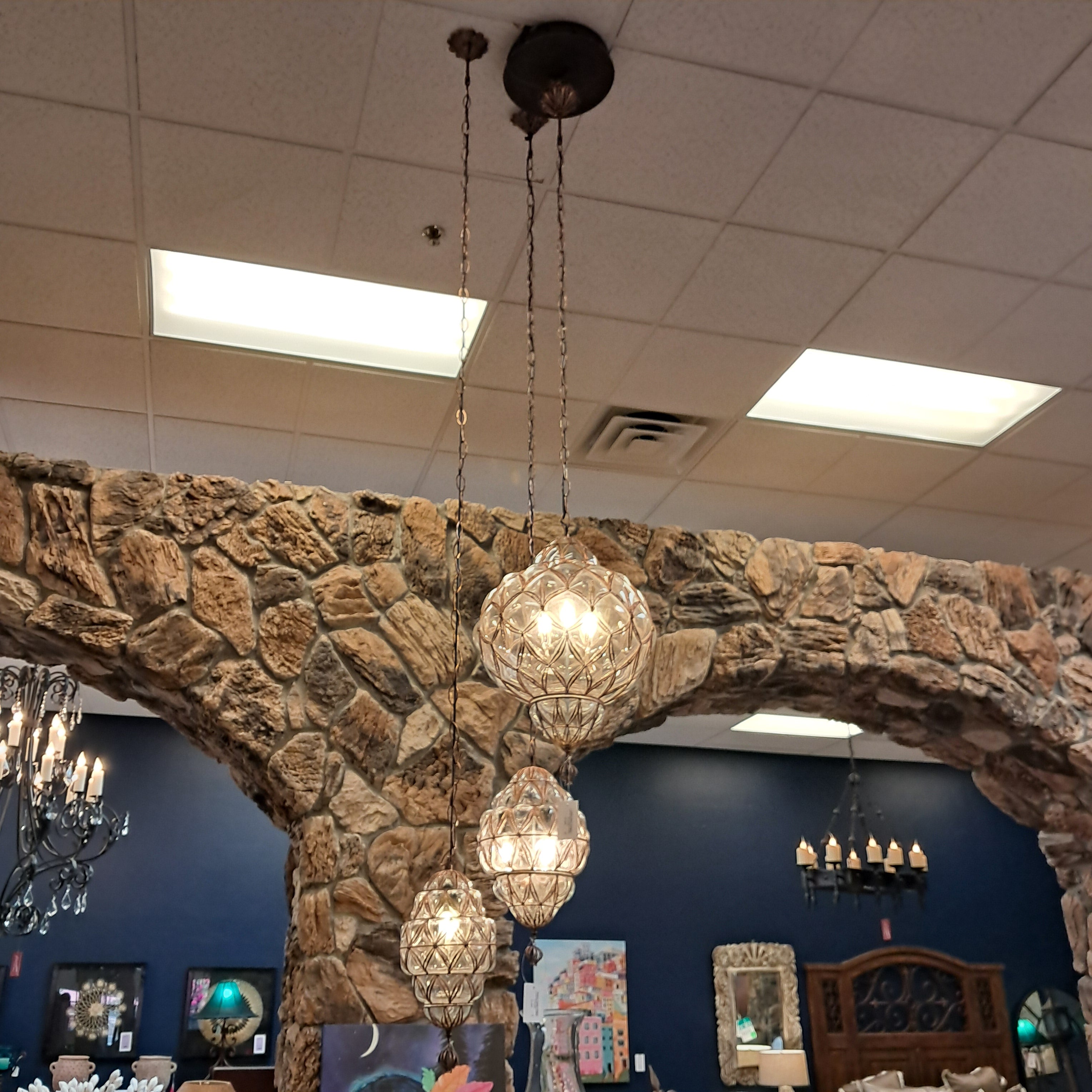 Chandelier hanging from a stone archway in a room with various decor items on the wall.