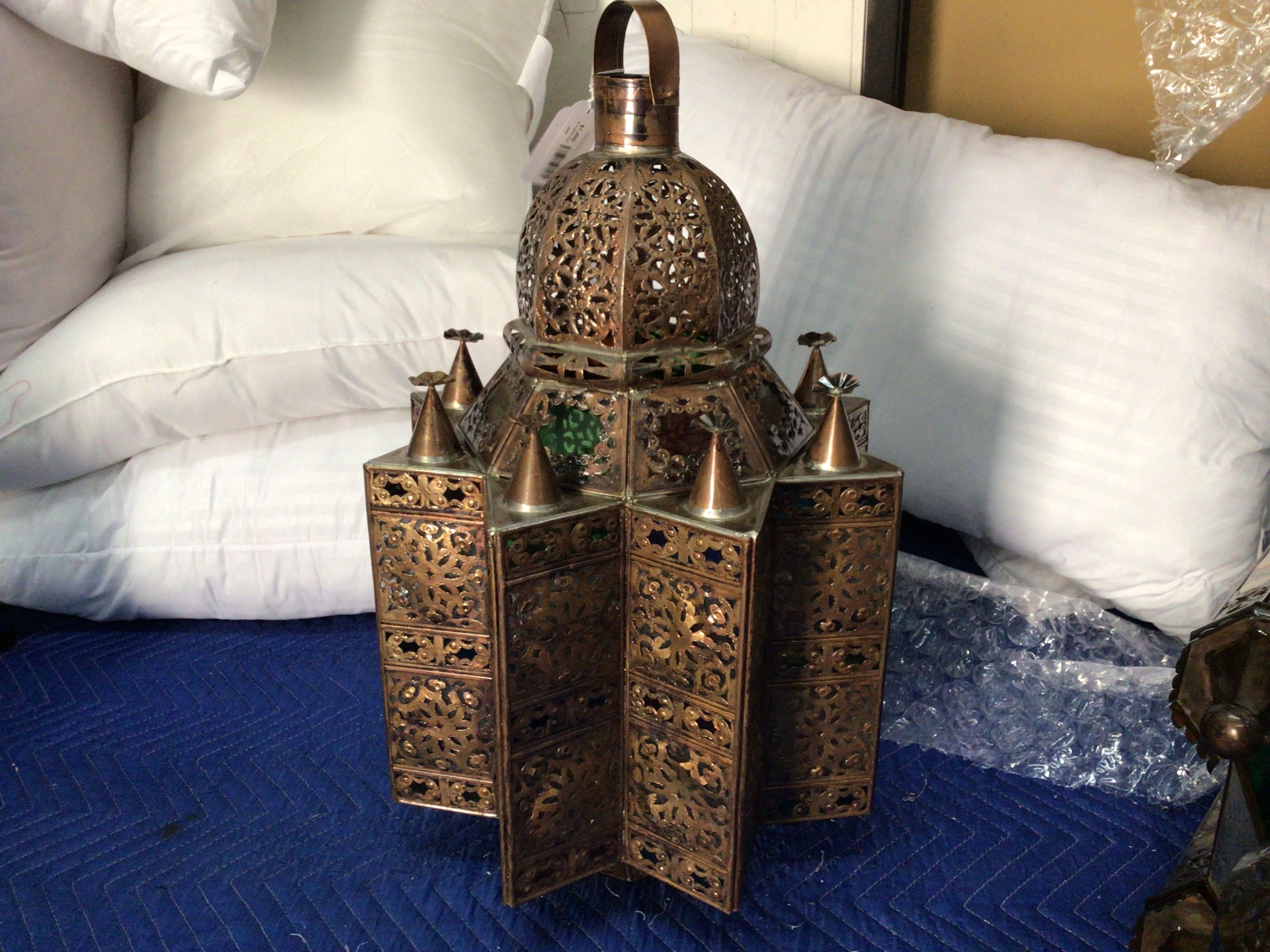 Decorative metal lantern on a blue surface with white pillows in the background
