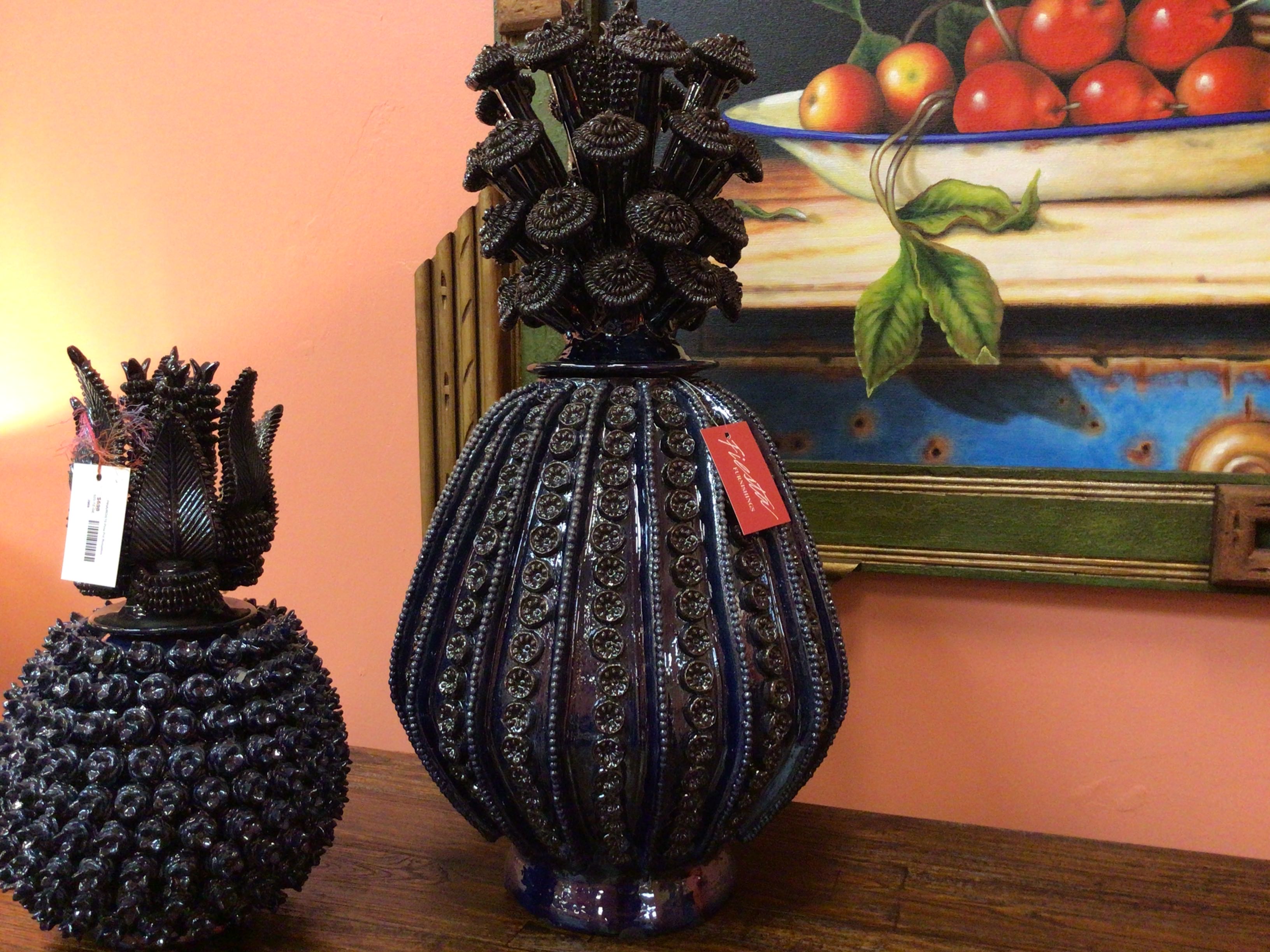 Decorative black vases with intricate designs on a wooden surface, with a painting of fruits in the background.