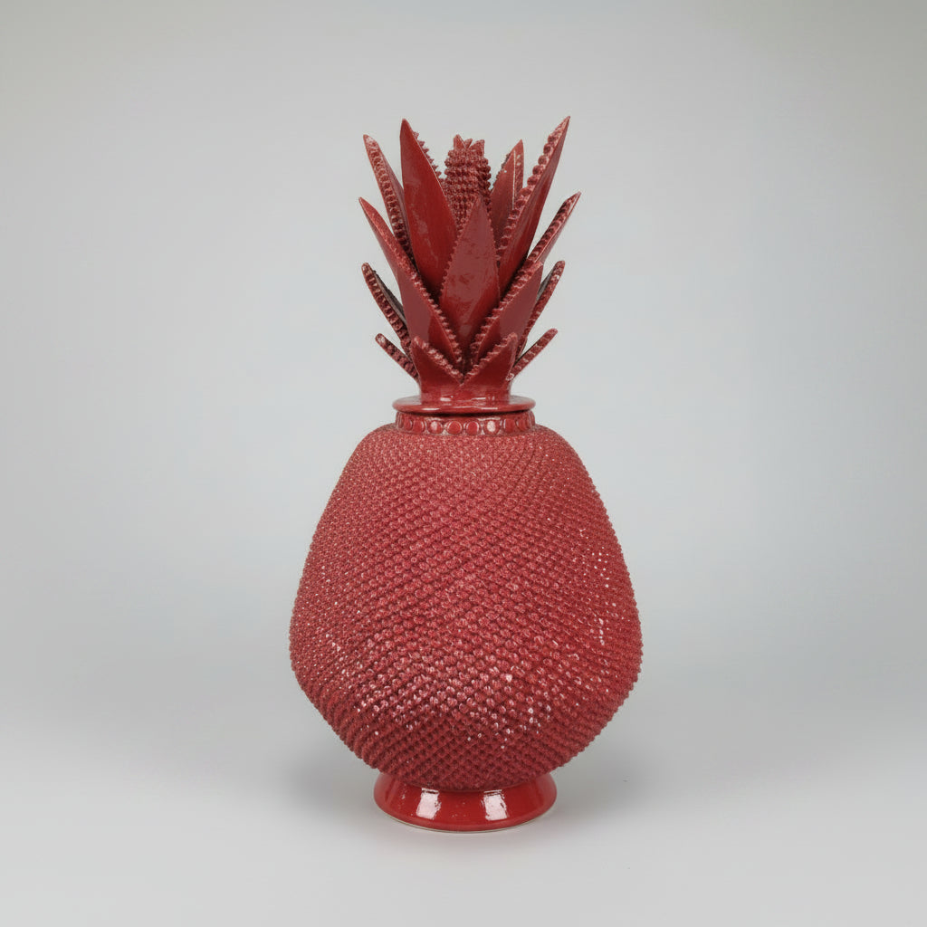 Decorative red vase with textured surface on a table next to a wooden deer figure and colorful painting.