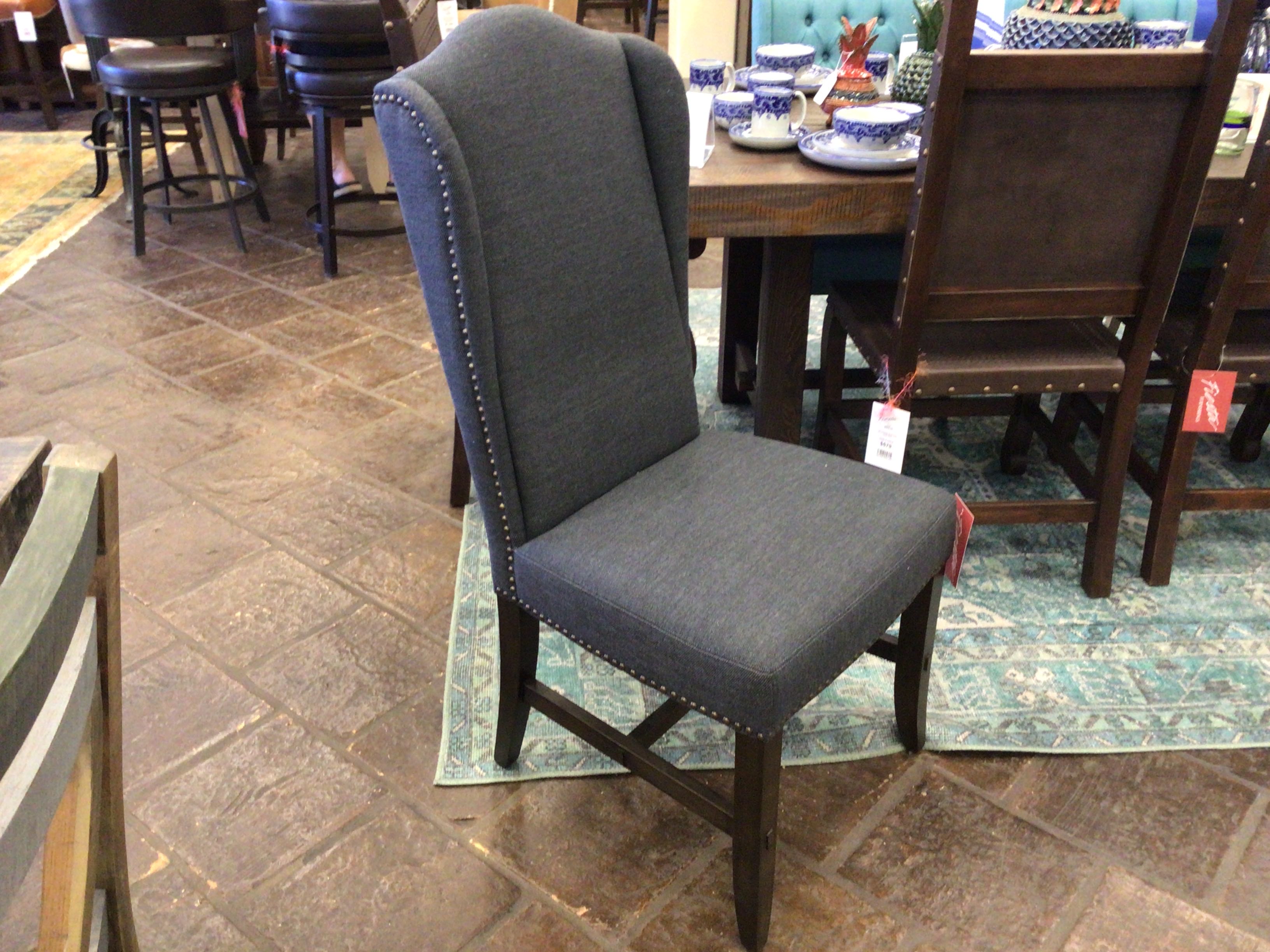 Gray upholstered chair with wooden legs on a stone floor, with a dining table and chairs in the background.