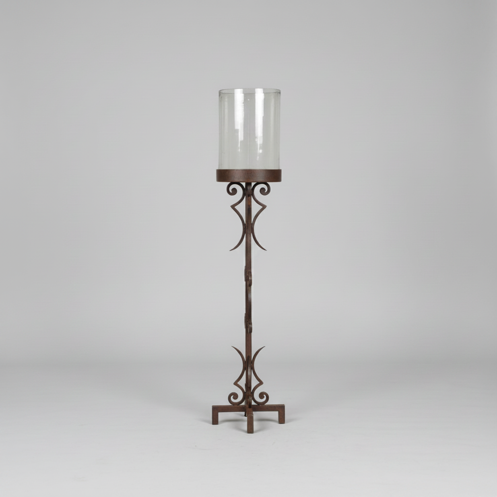A tall wrought iron candlestick holder with a twisted stem design and a clear glass cylinder shade, photographed against a neutral light gray background.