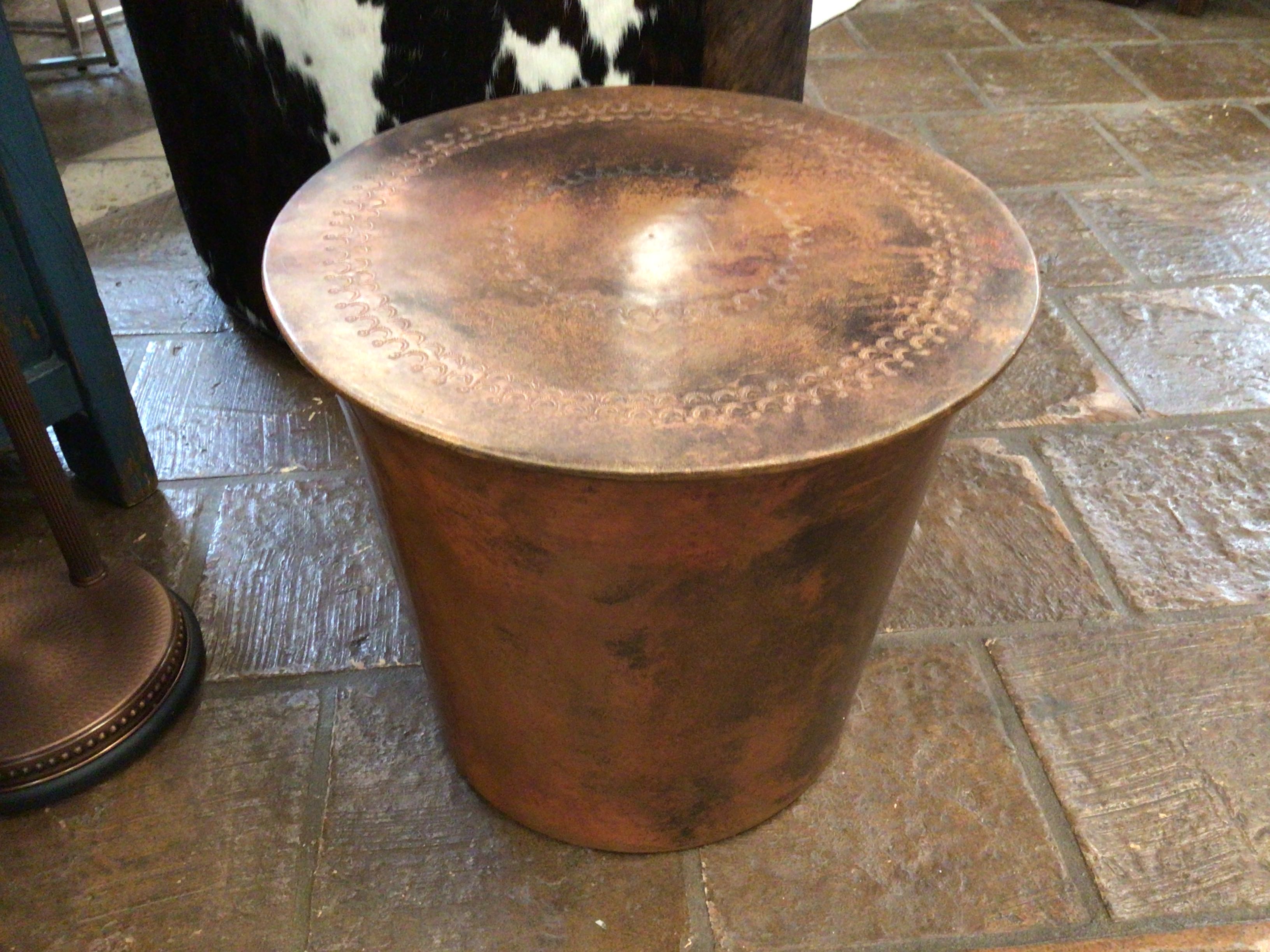 Copper side table on a stone floor with a cow partially visible.