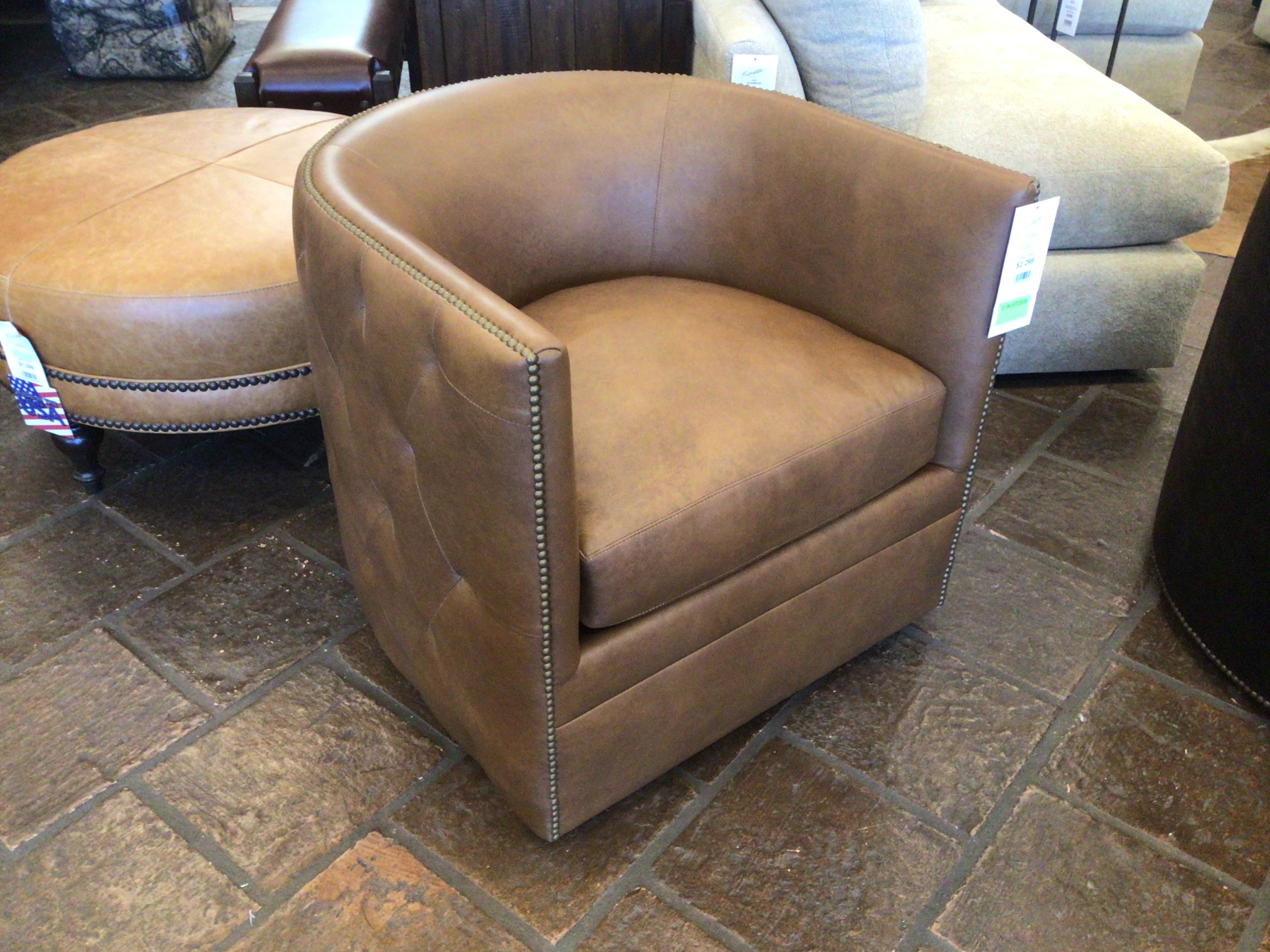 Brown leather armchair in a showroom setting with tiled floor and other furniture.
