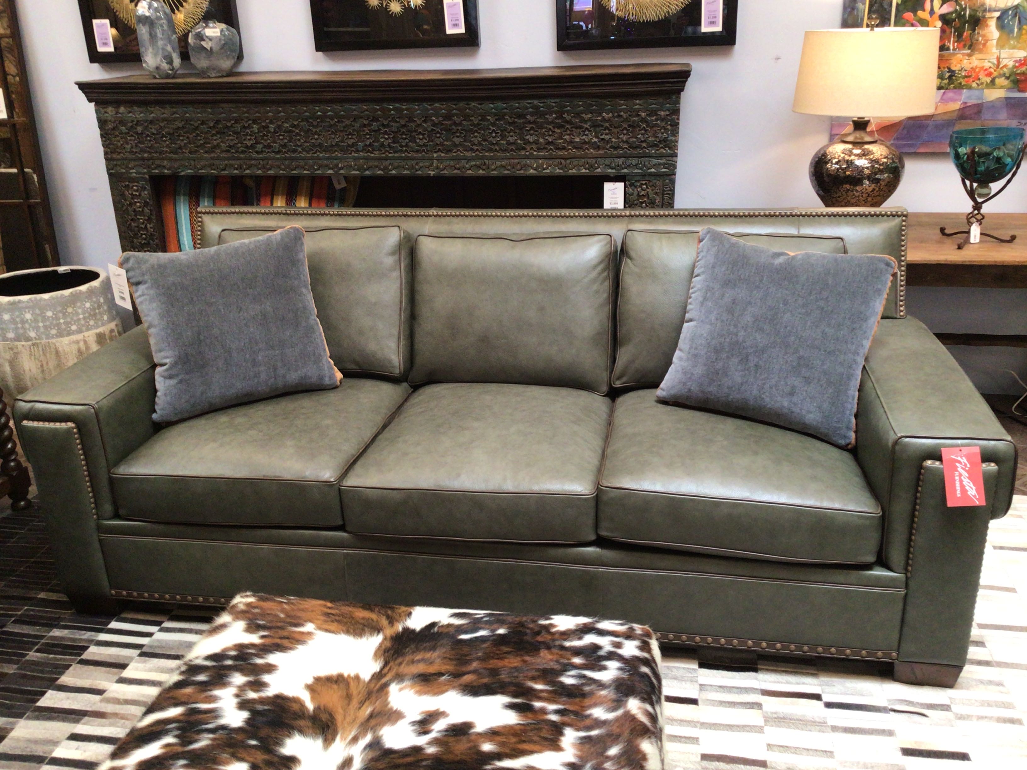 Green leather sofa with gray pillows in a room setting.