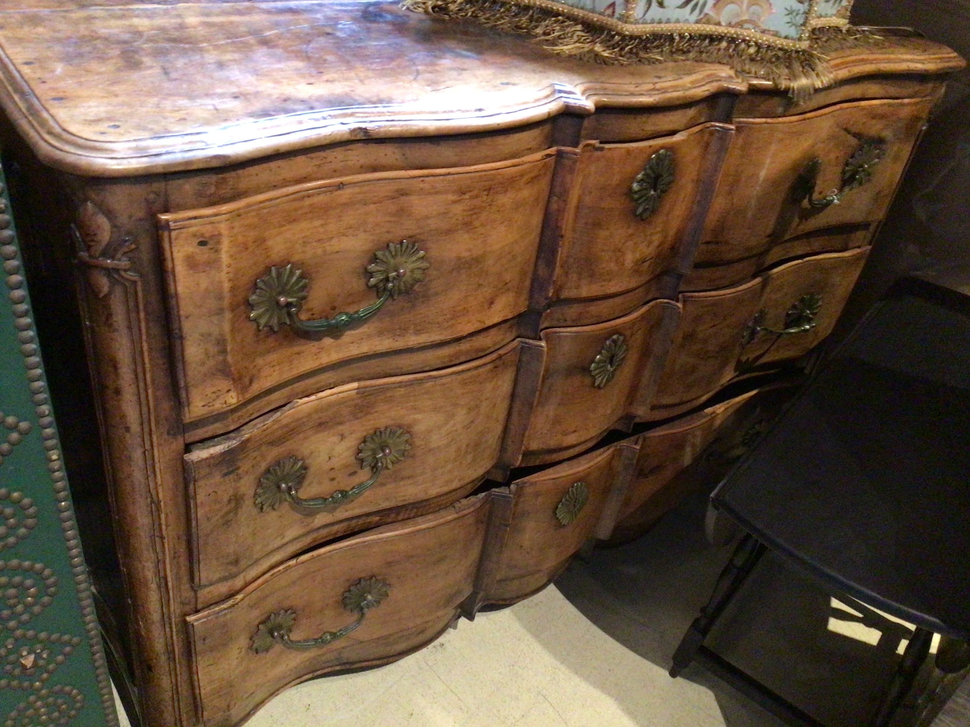 Wooden dresser with curved design and brass handles in a room setting.