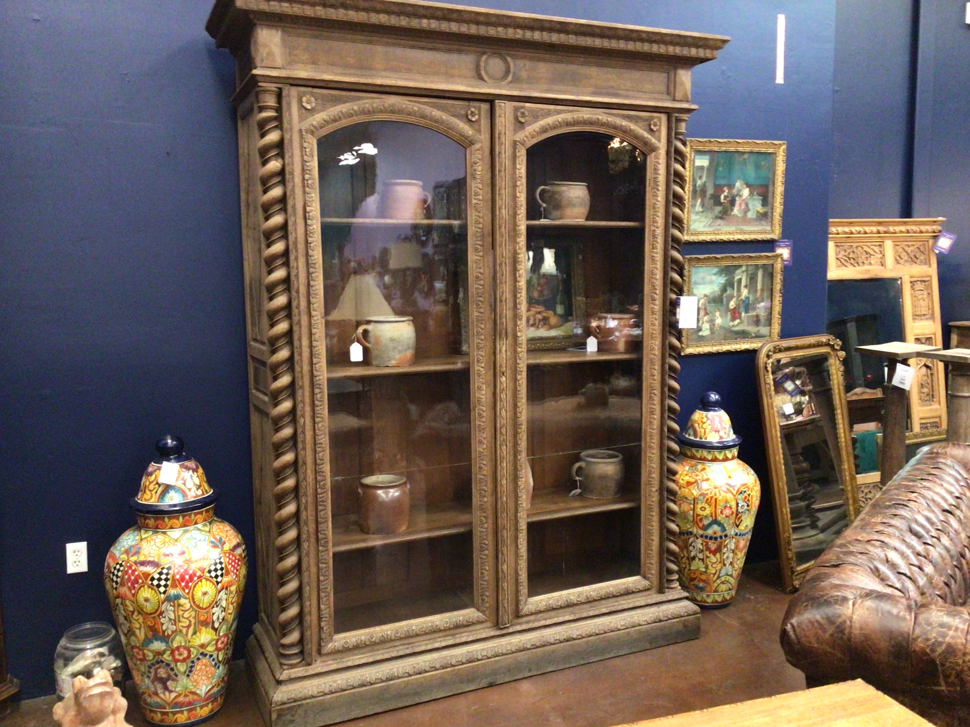 Decorative wooden cabinet with glass doors against a blue wall, surrounded by decorative items.