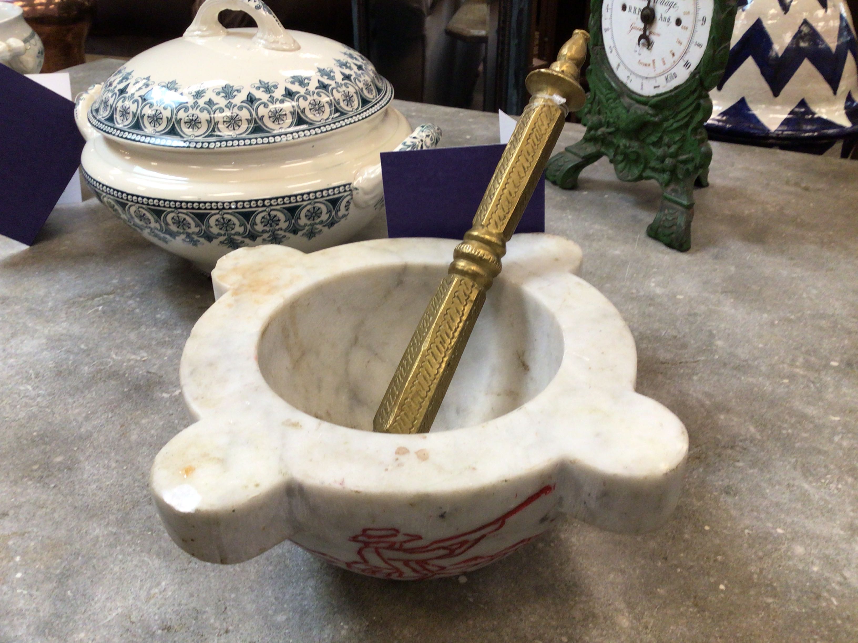 Marble mortar and pestle with a brass pestle on a concrete surface, with decorative items in the background.
