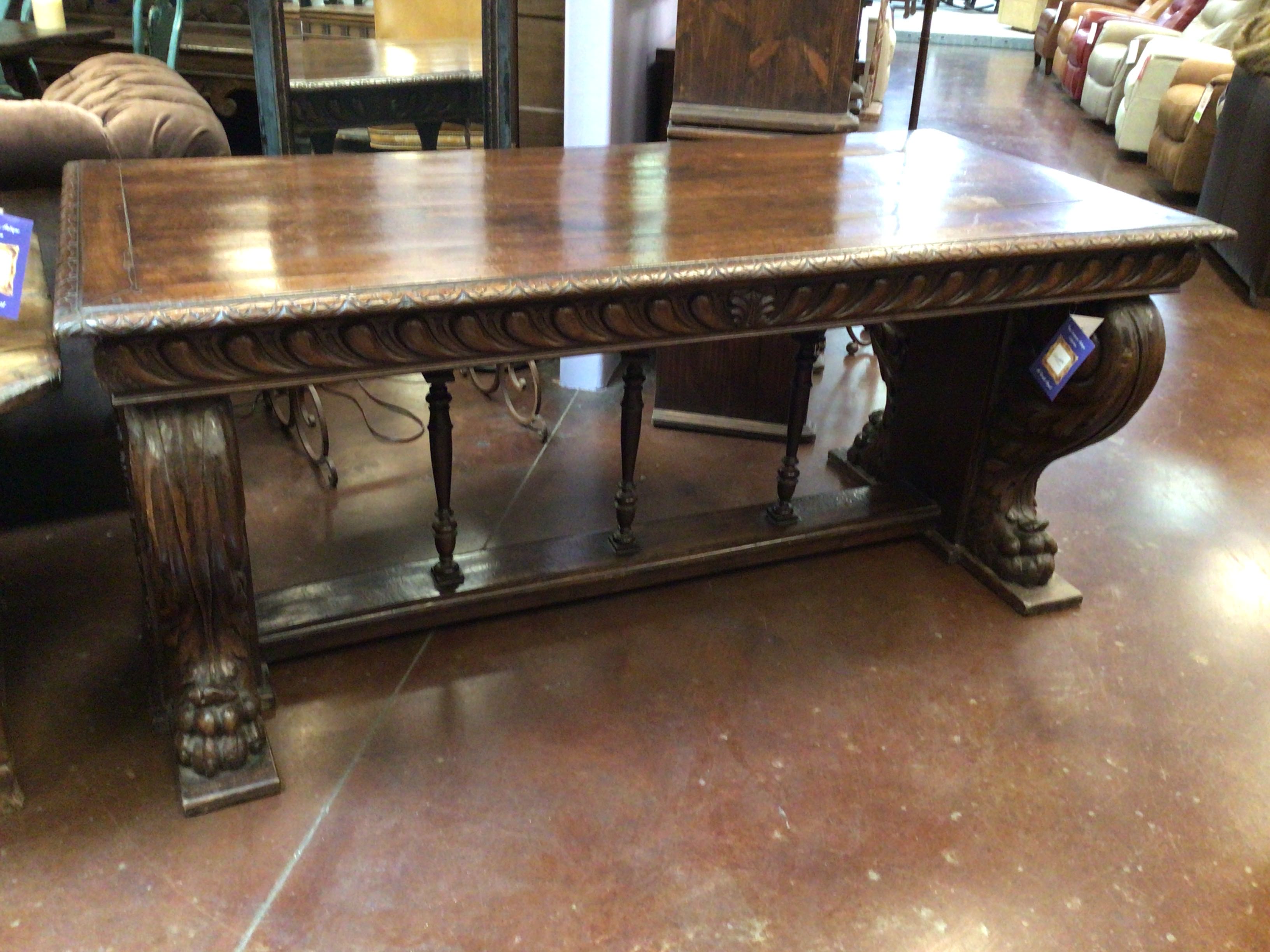 Large wooden table with intricate carvings in a store setting