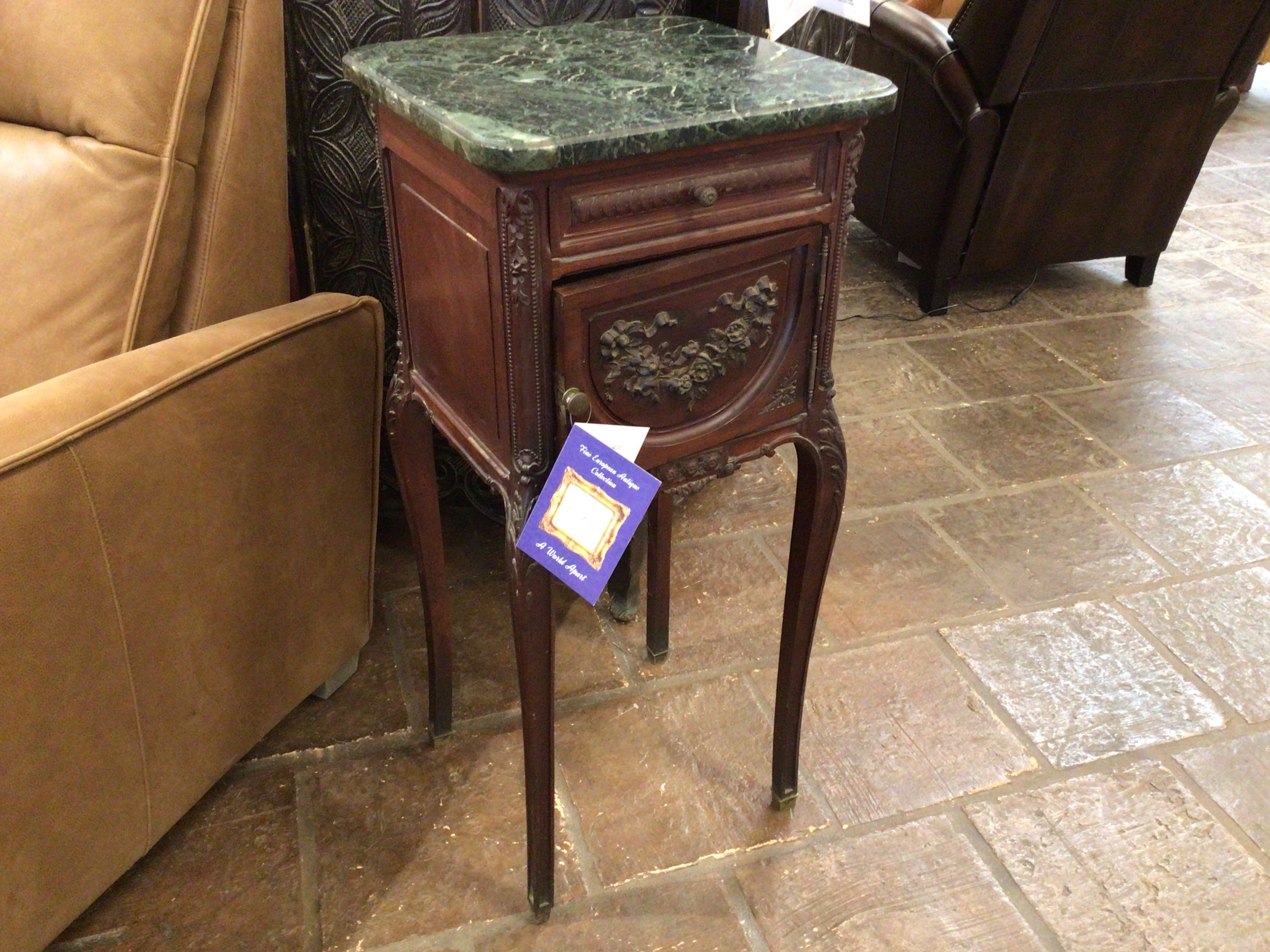 Wooden side table with marble top in a room with furniture and a stone floor.