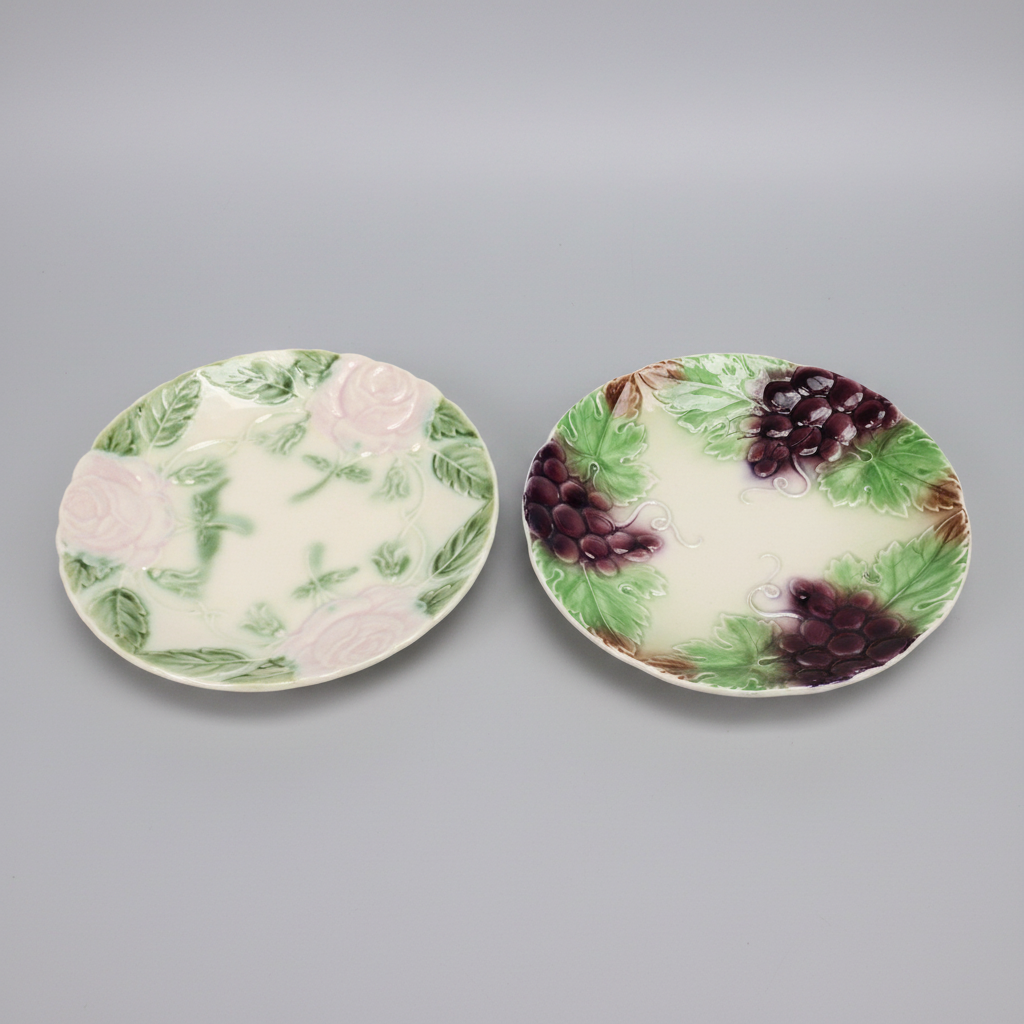 Two ceramic plates with floral and fruit designs on a gray background