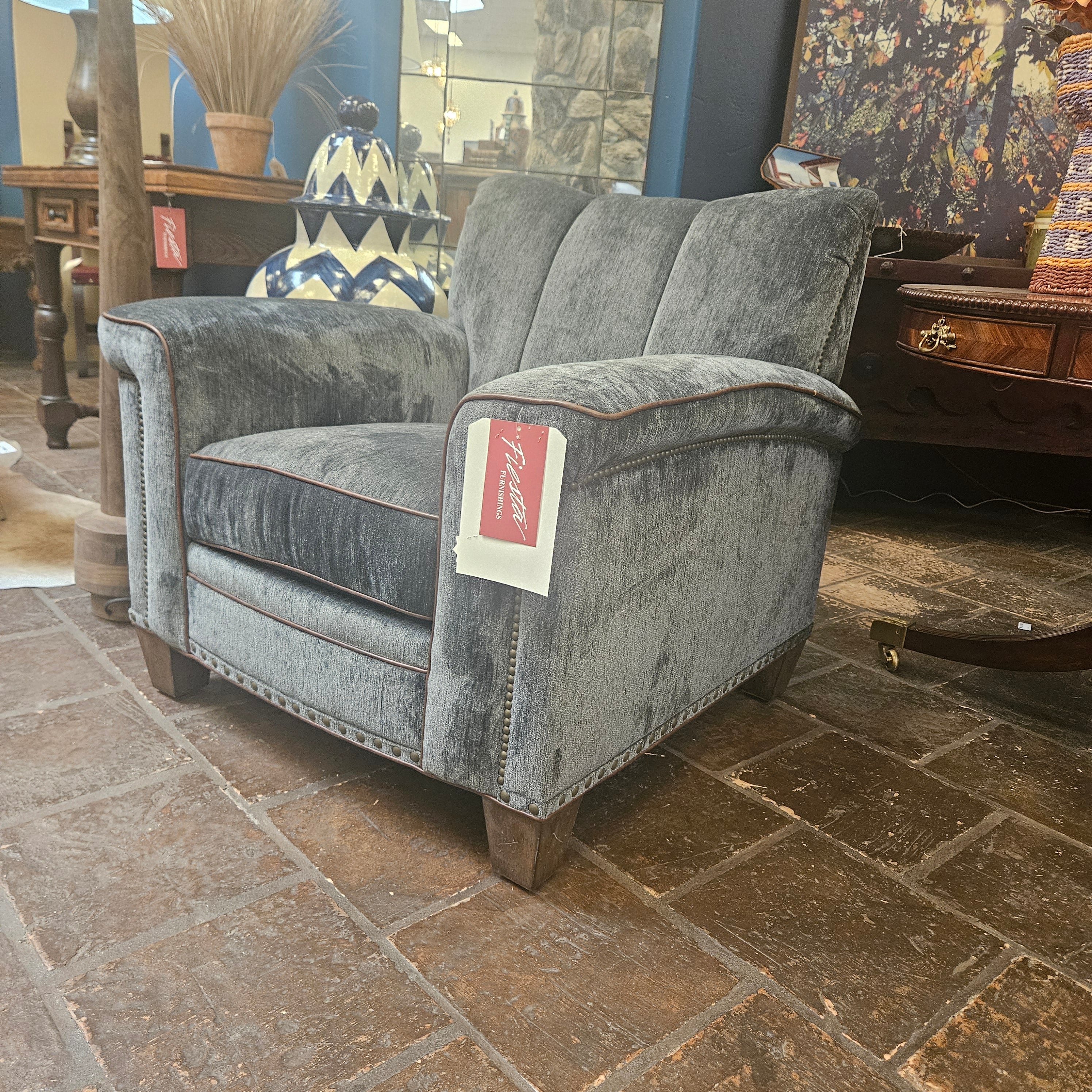 Gray upholstered chair with a visible brand label against a stone wall.