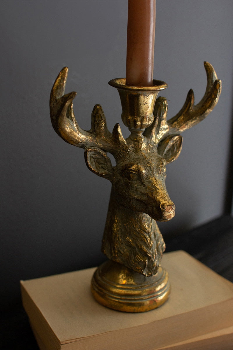 Gold deer head candle holder with a brown candle on a dark background