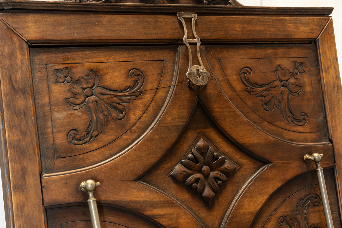 Close-up of an antique dark brown wooden cabinet door featuring intricate hand-carved floral scrollwork and a central diamond-shaped relief, with brass-toned hardware visible.