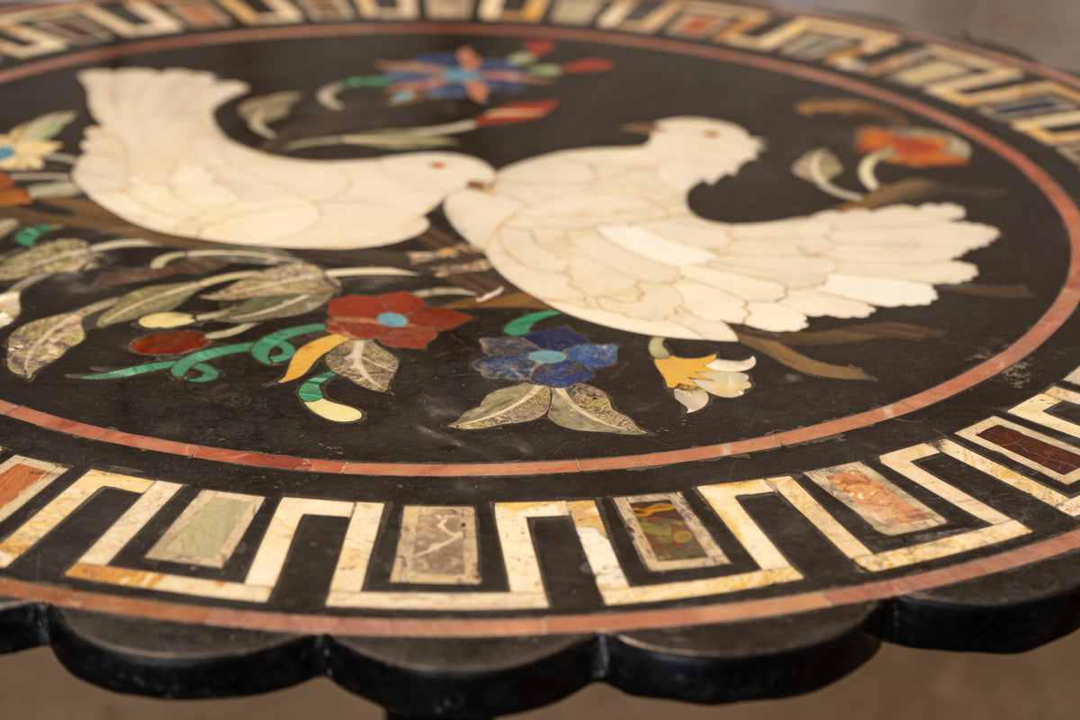 Close-up of an ornate round table top featuring a black inlay background with a white dove motif and colorful floral accents, plus geometric border details.