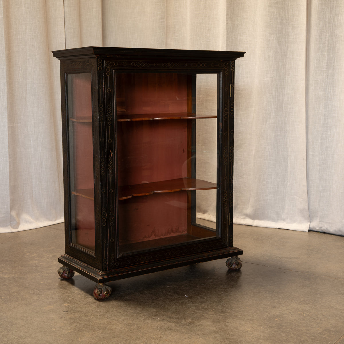 A dark wood display cabinet with glass doors and shelves, mounted on casters, photographed against a draped fabric backdrop.