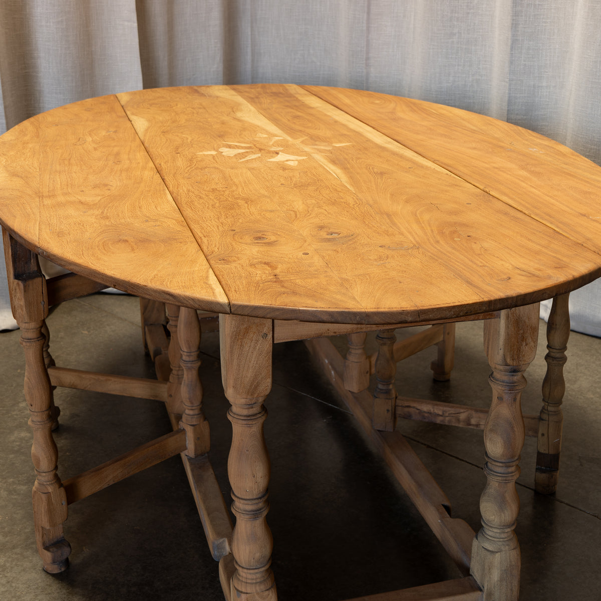 An oval wooden drop-leaf table with turned legs and stretchers, shown with the center leaf open to reveal the interior. The tabletop and frame have a warm natural wood finish with visible grain and knots.