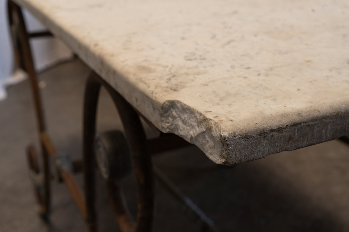 Close-up of a rustic vintage workbench with a thick, heavily worn beige stone or concrete top and a dark metal frame with wheels.
